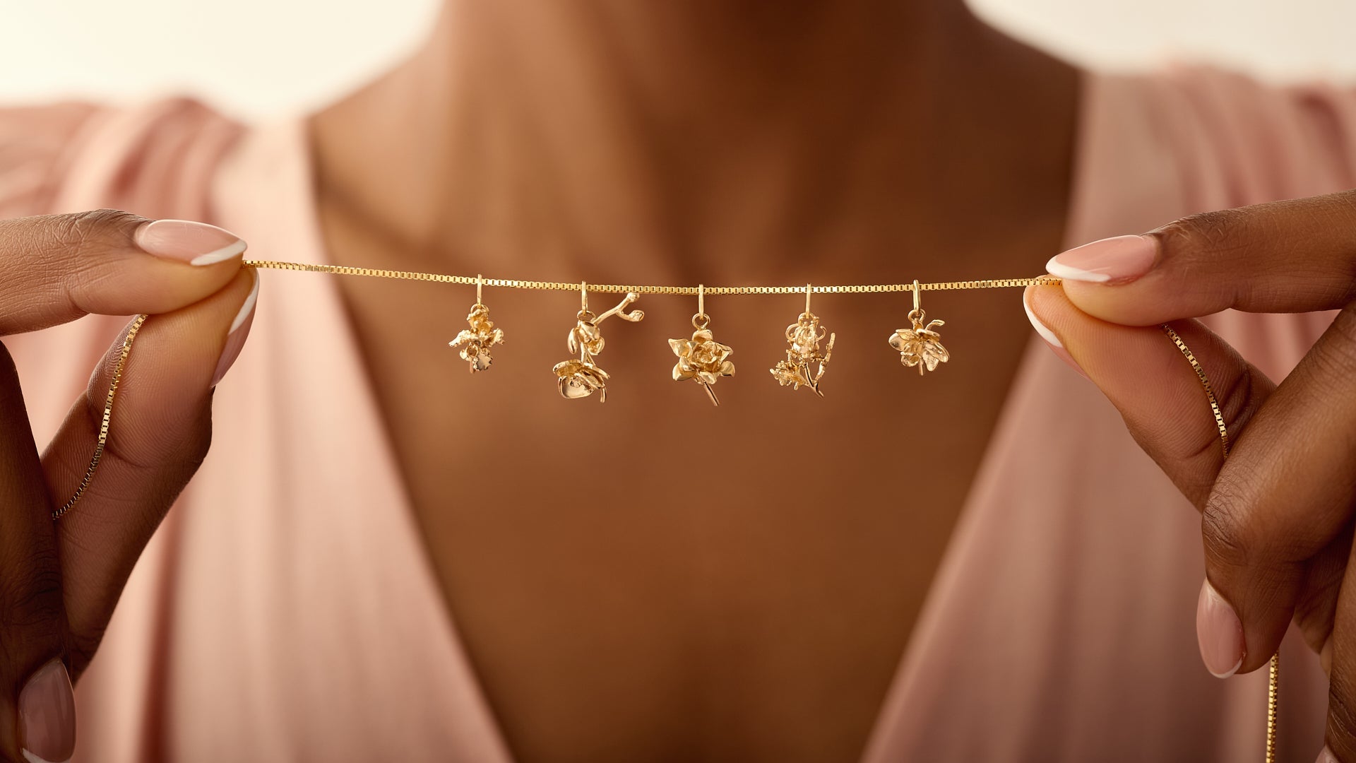 woman holding flower charms lined up on gold chain in pink dress
