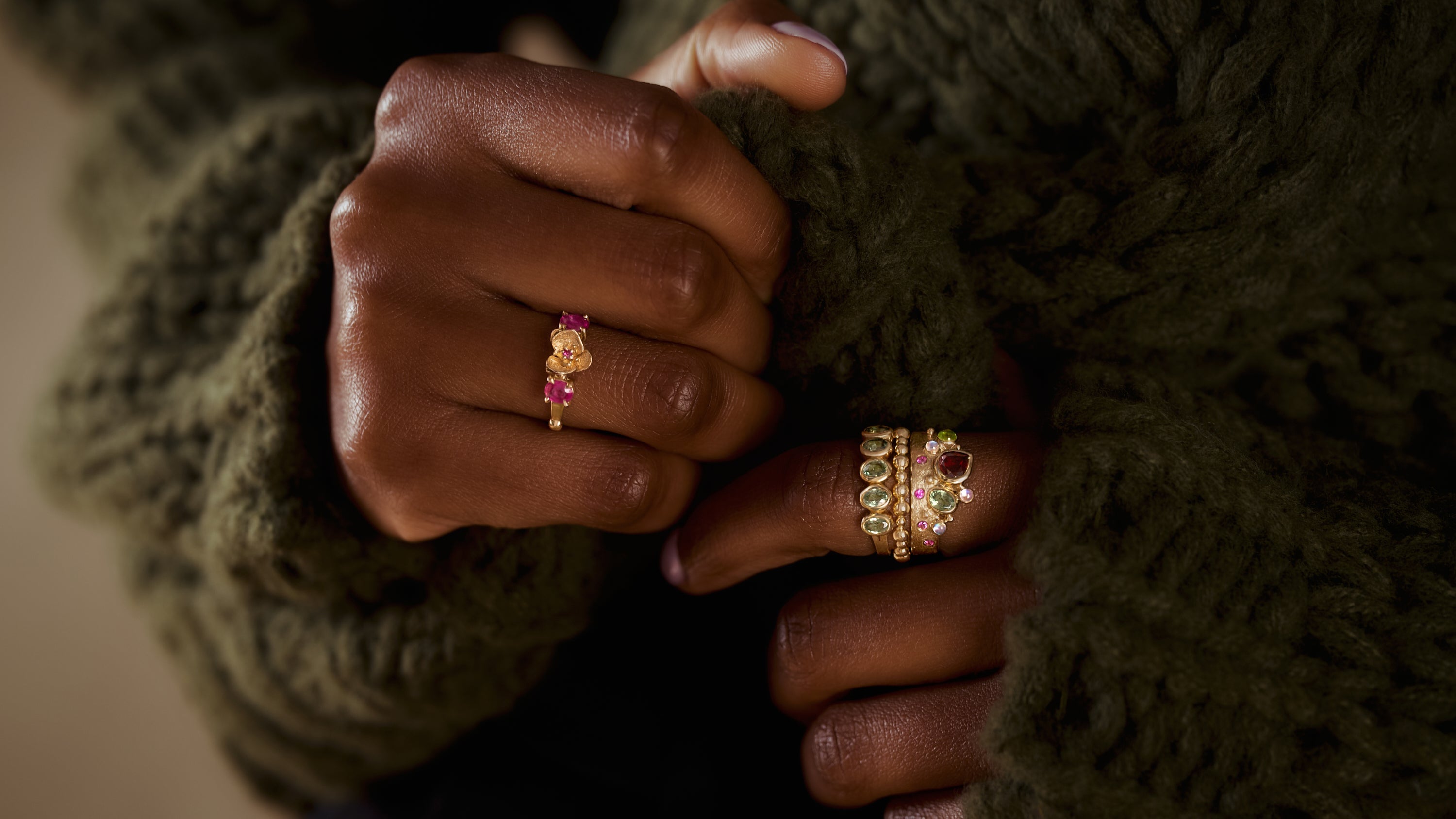 Woman wearing multiple colorful gemstone and gold rings with green sweater