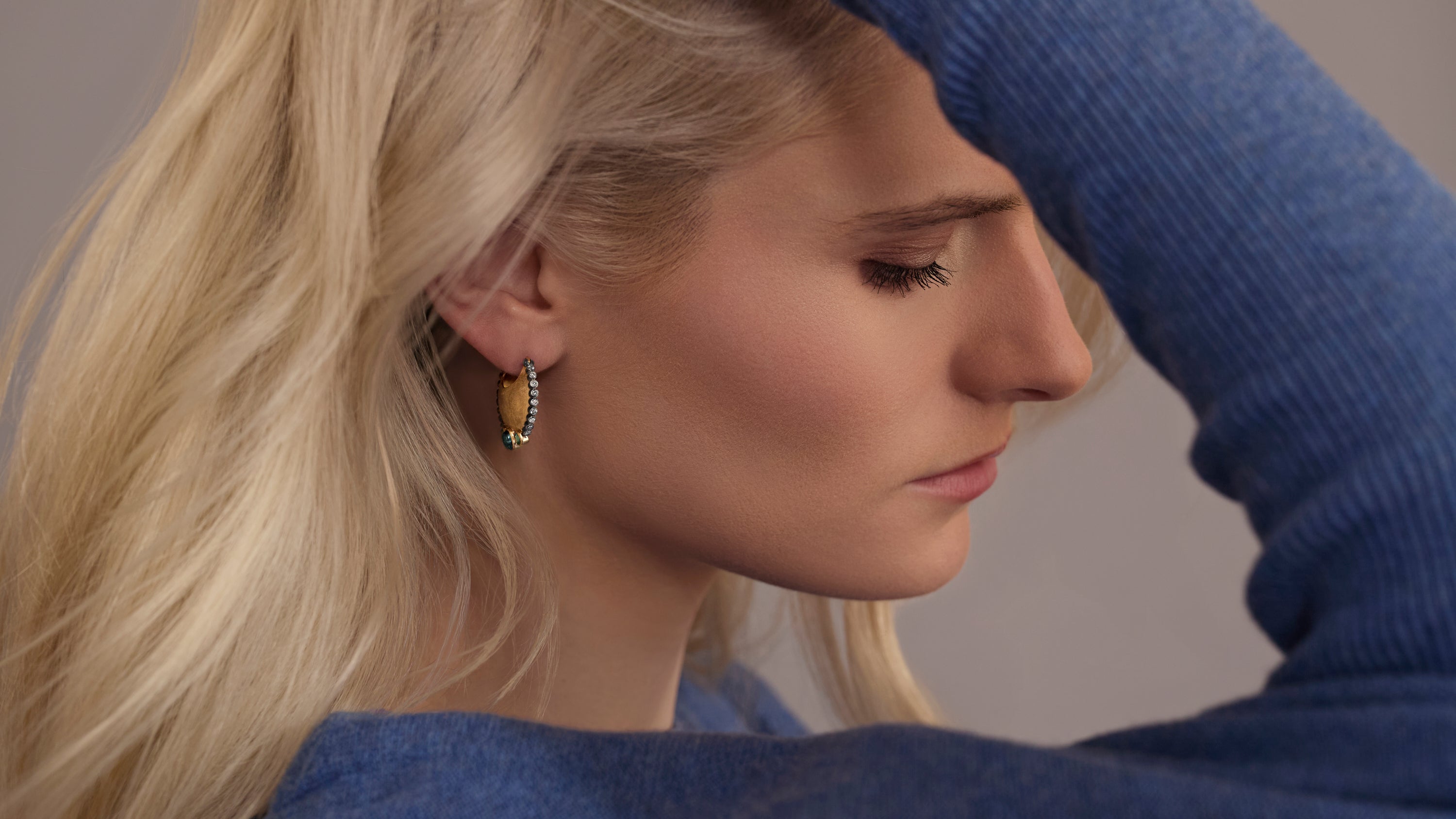 Woman in blue sweater and gold hoops with diamond encrusted edge