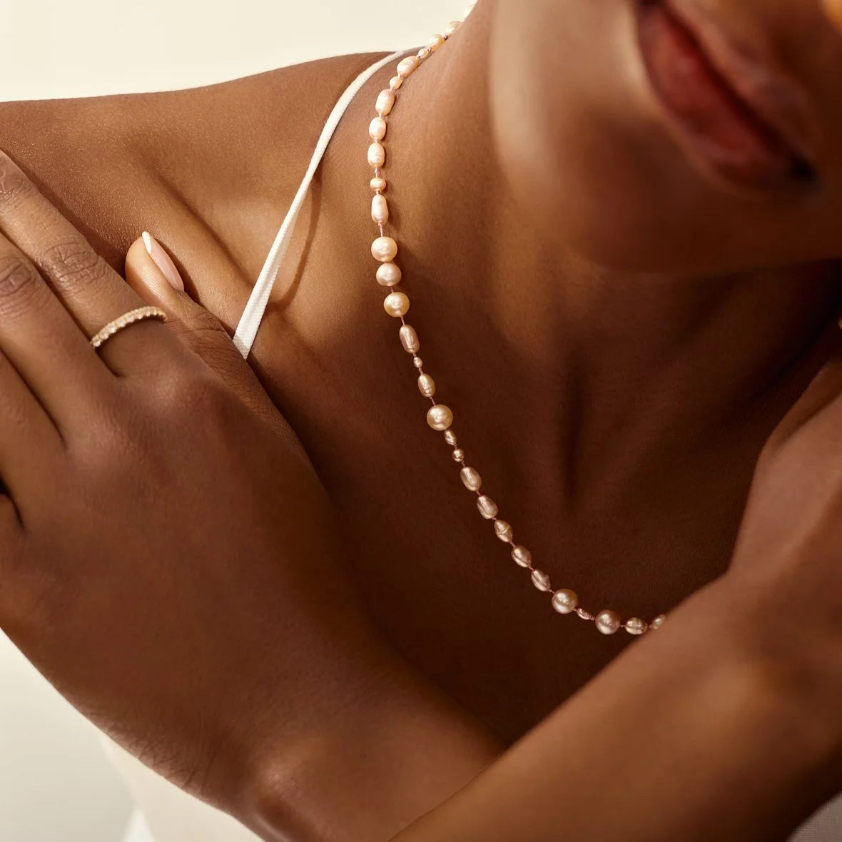 Close-up of a person wearing a pearl necklace with a neutral background