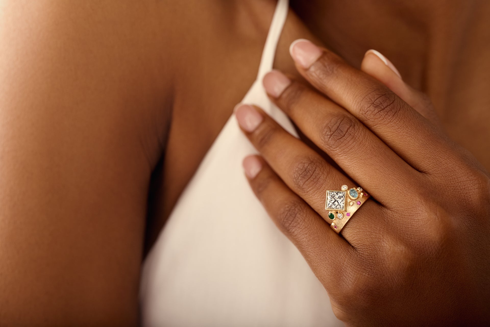 Close-up of a hand wearing a gold ring with a diamond on a blurred background