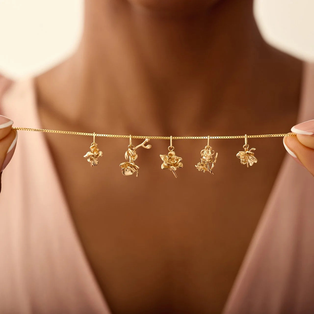 Gold necklace with floral charms held by a person against a neutral background