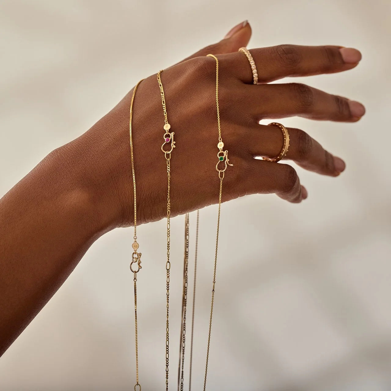 Hand wearing gold jewelry with a neutral background