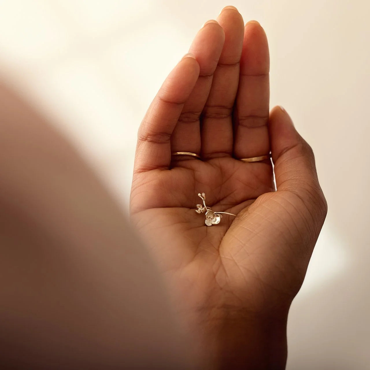 Small silver charm held in the palm of a hand against a neutral background