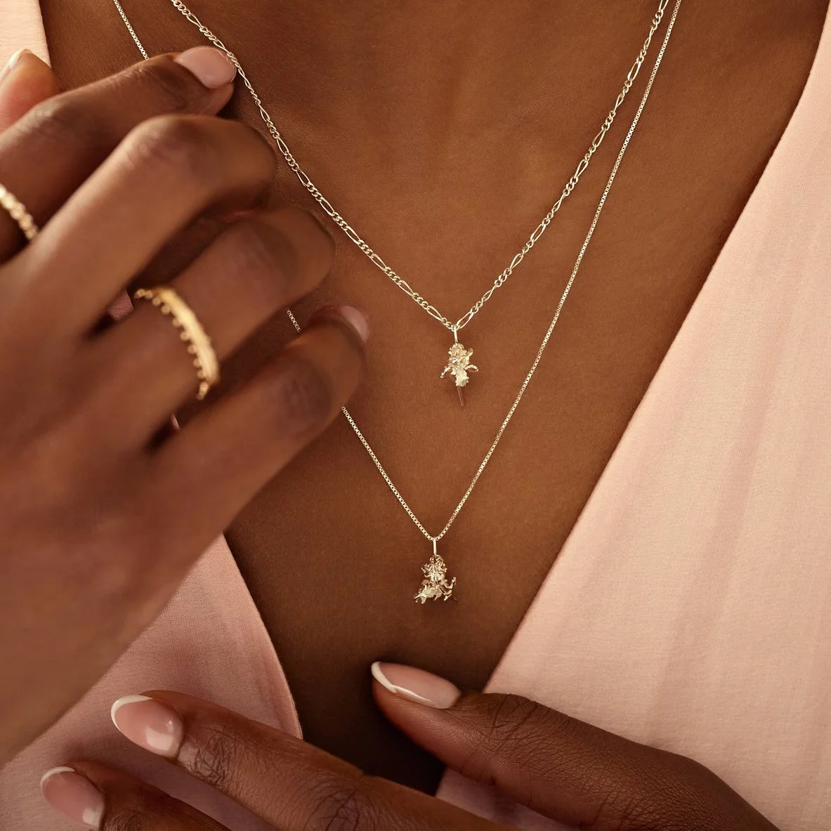 Close-up of a person wearing two silver necklaces with pendants on a neutral background