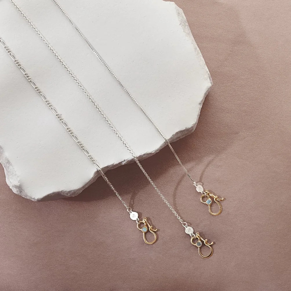 Three necklaces with gold clasps on a beige surface