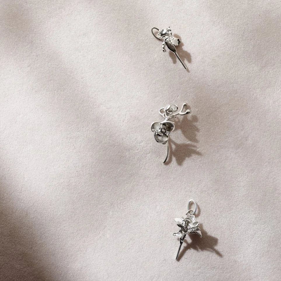 Three silver floral charms on a light pink background