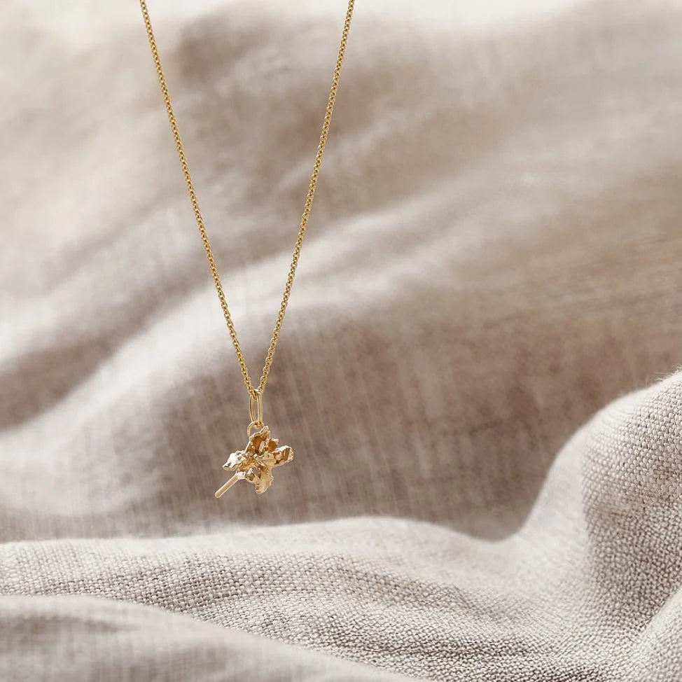 Gold necklace with a small pendant on a textured beige fabric background