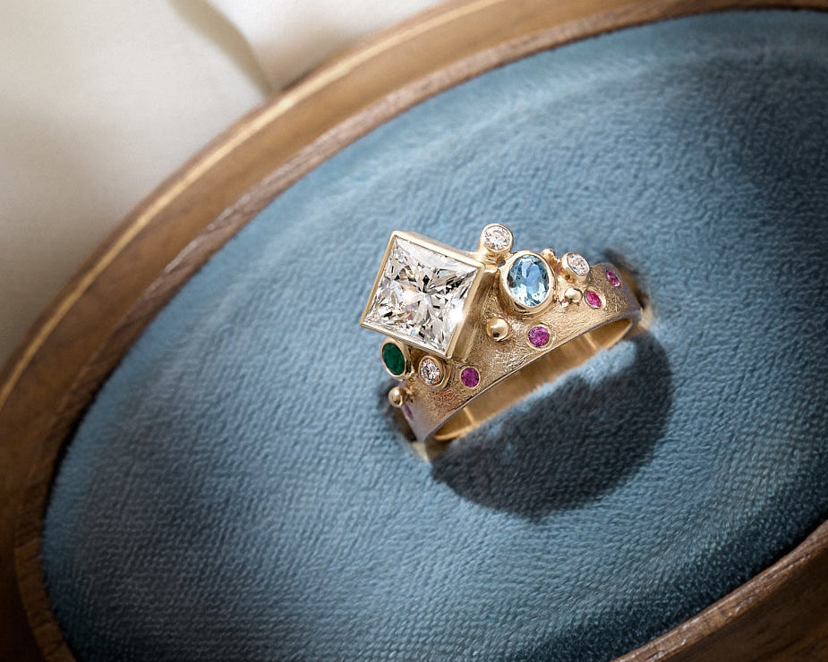 Gold ring with gemstones on a blue cushion inside a wooden box