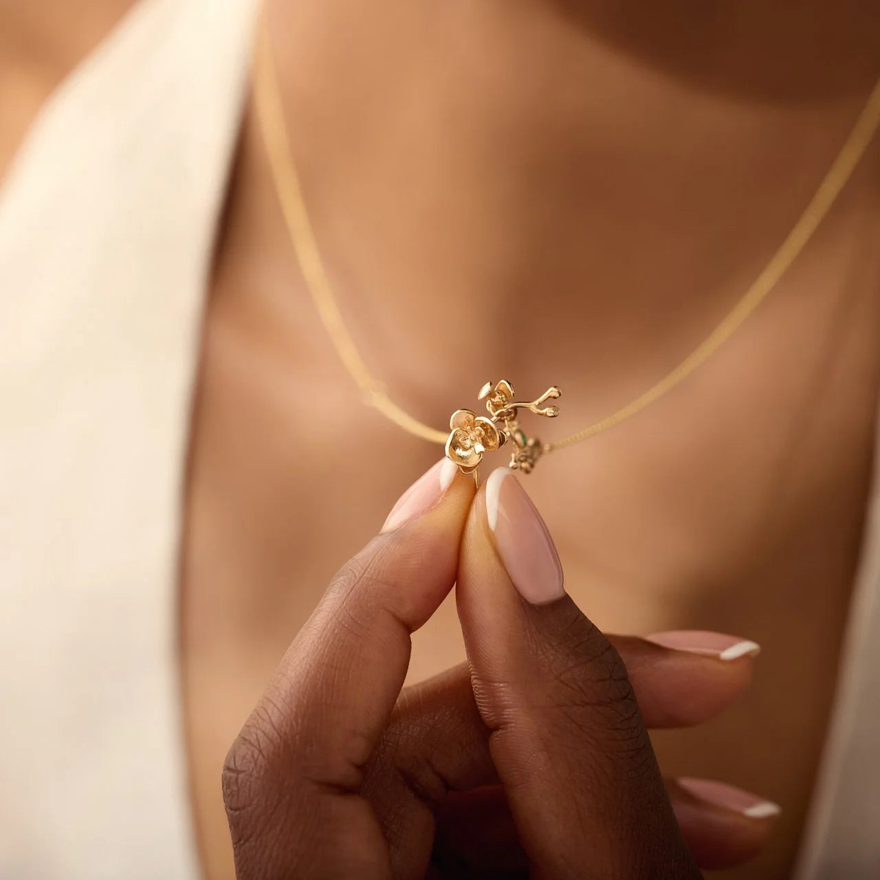 Gold necklace with a floral pendant held by a hand against a blurred background