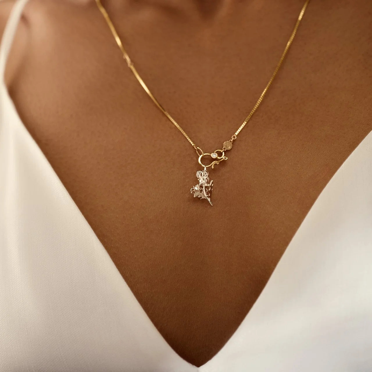 Gold necklace with a pendant on a person wearing a white top