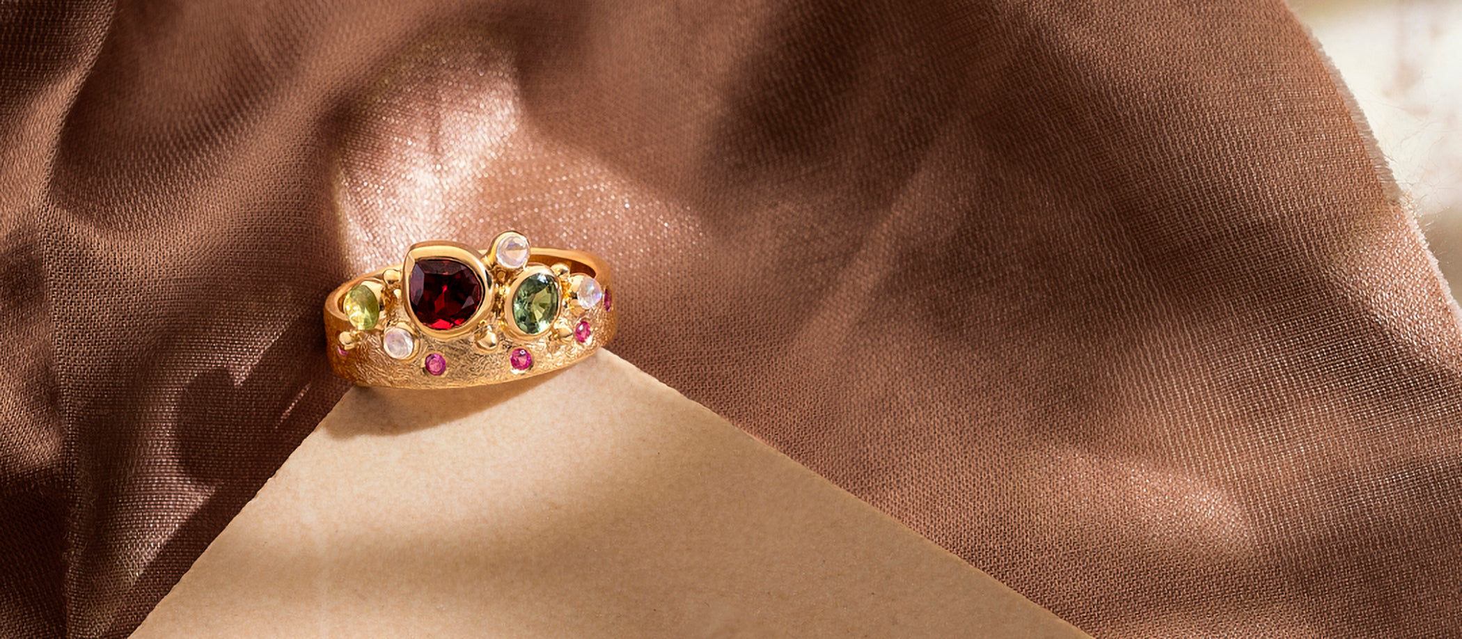 Gold ring with colorful gemstones on a brown fabric background