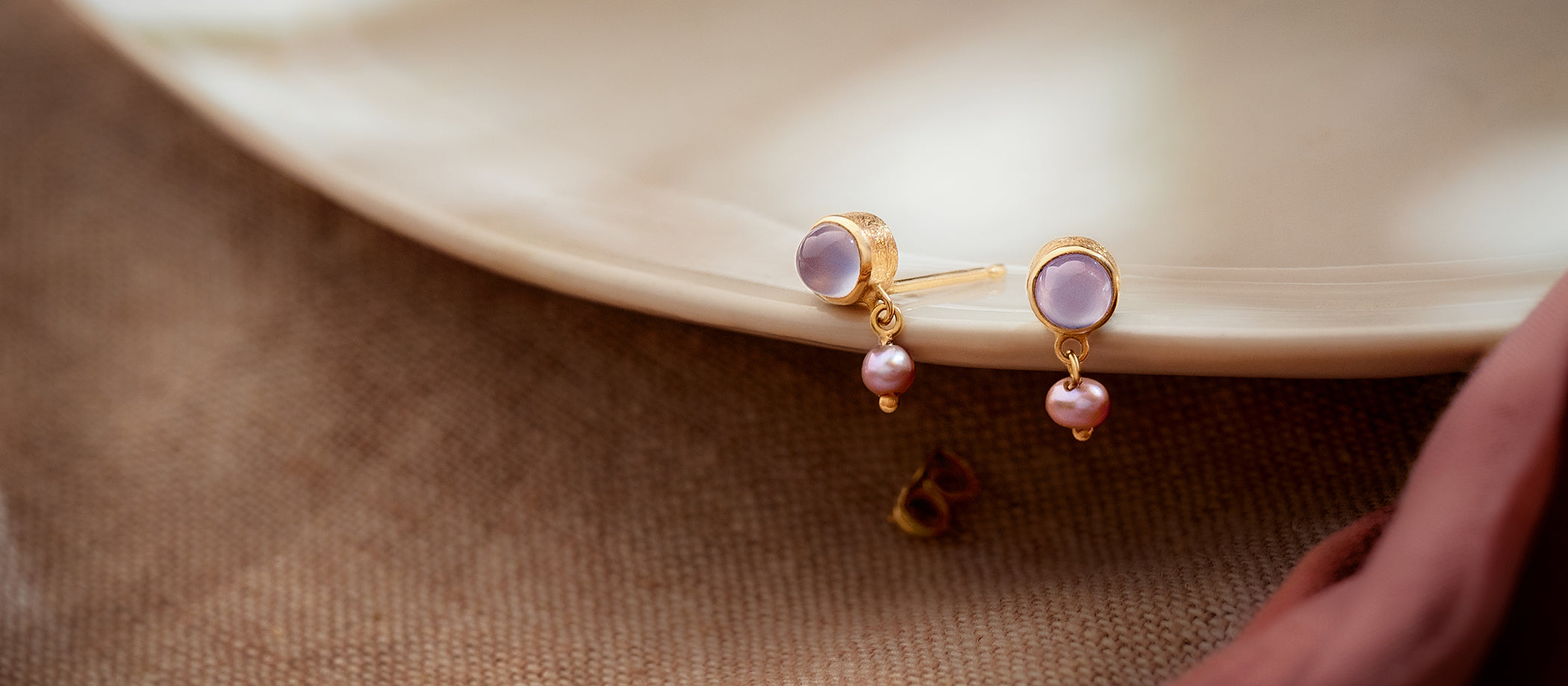 Pair of gold earrings with purple gemstones and pearls on a beige plate.