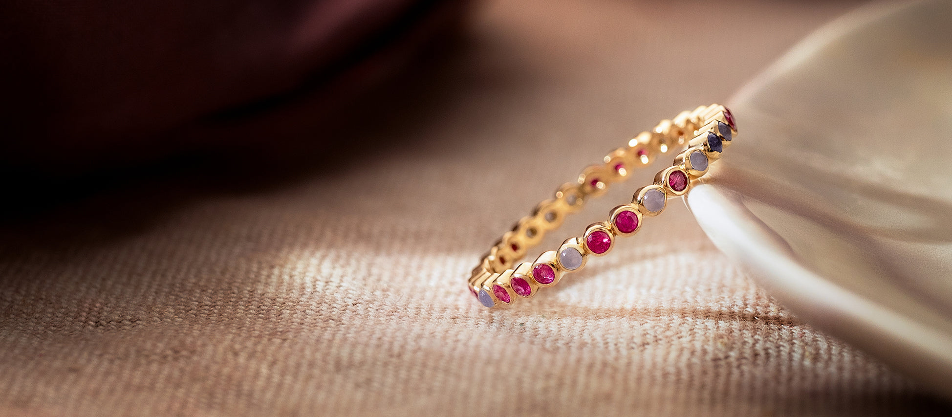 Gold ring with red and purple gemstones on a textured surface