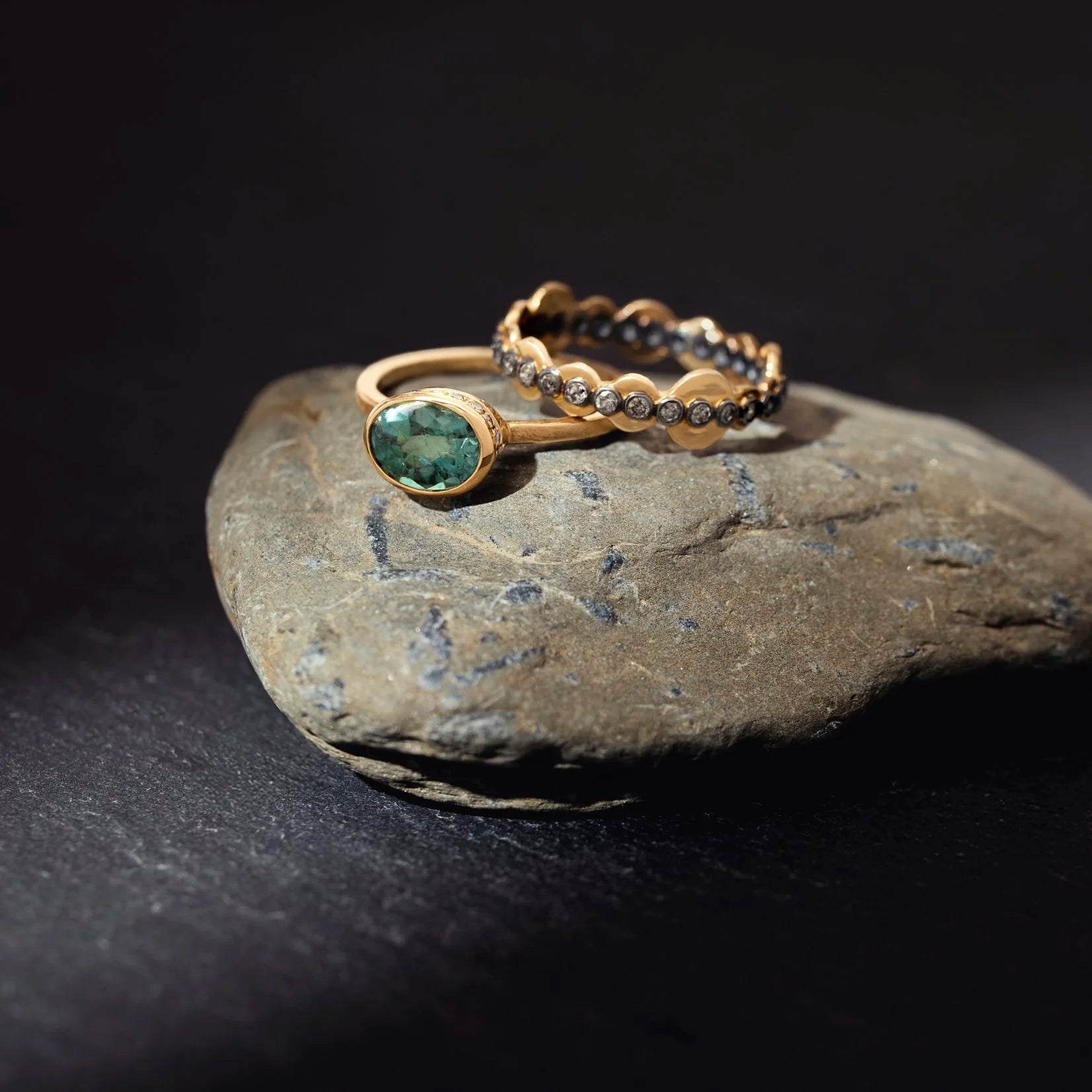 Two gold rings with gemstones on a dark stone surface