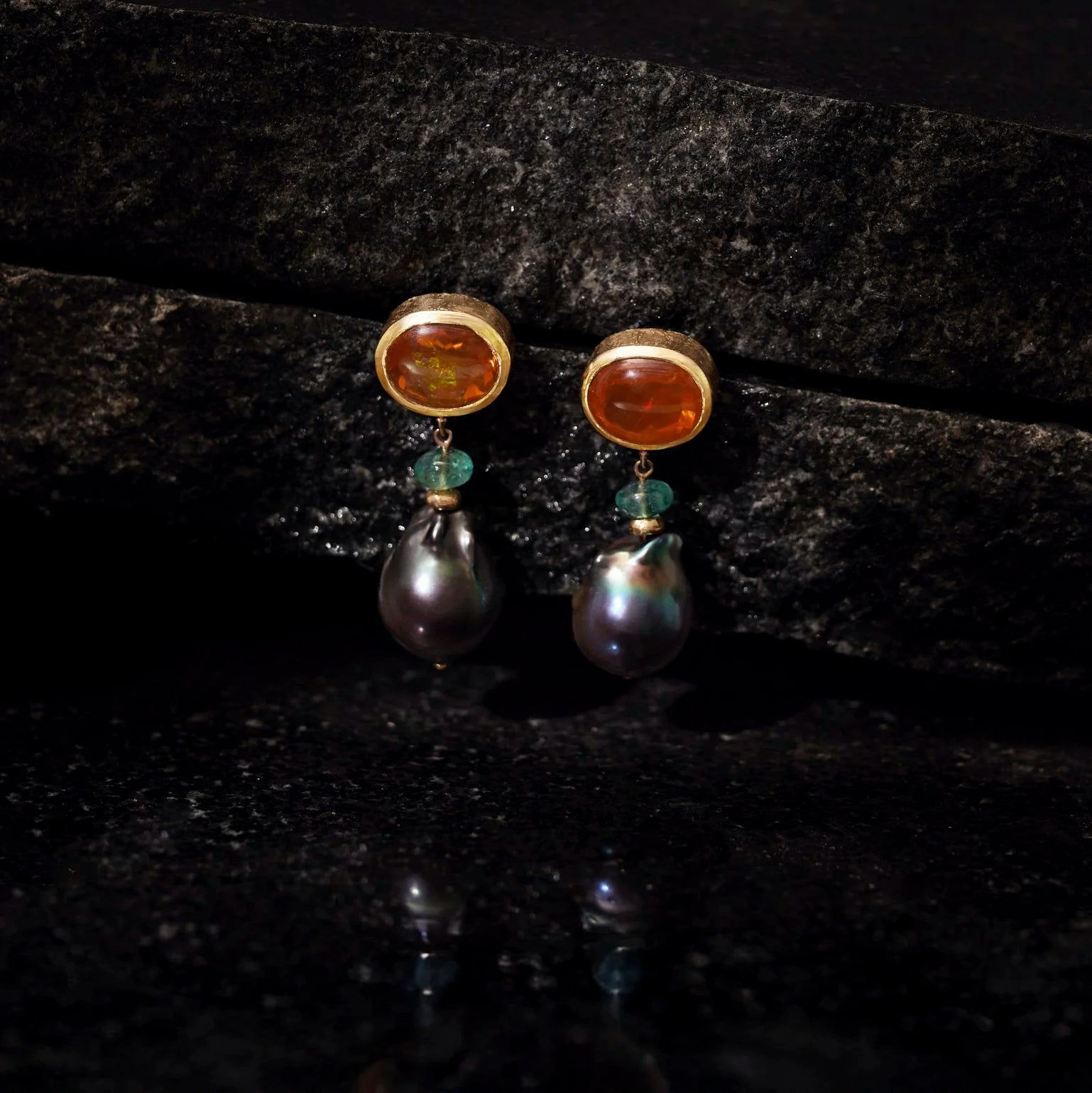 Pair of earrings with gemstones and pearls on a dark surface