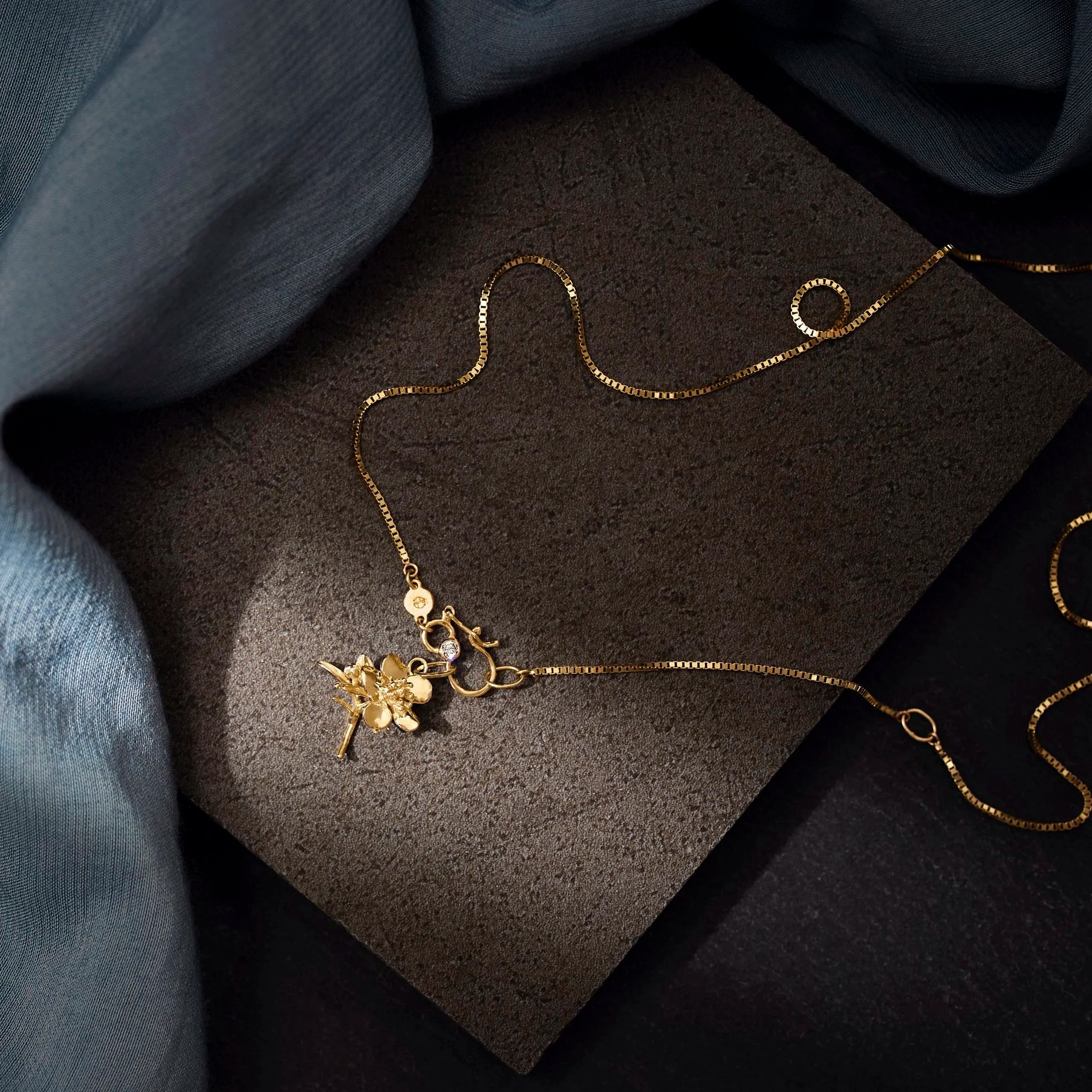 Gold necklace with floral pendant on a dark stone surface