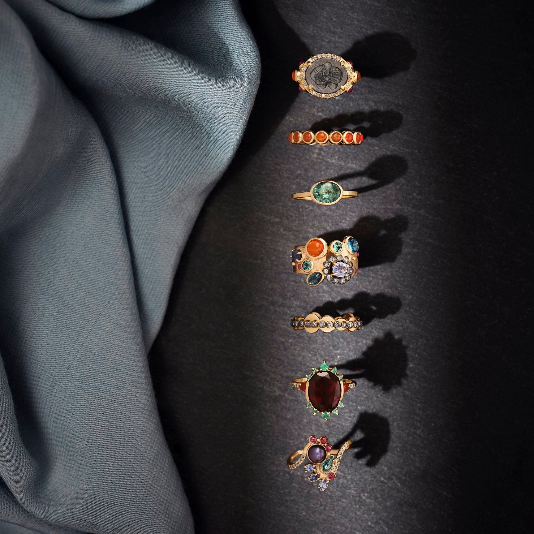 Set of gold rings with various gemstones on a dark fabric background