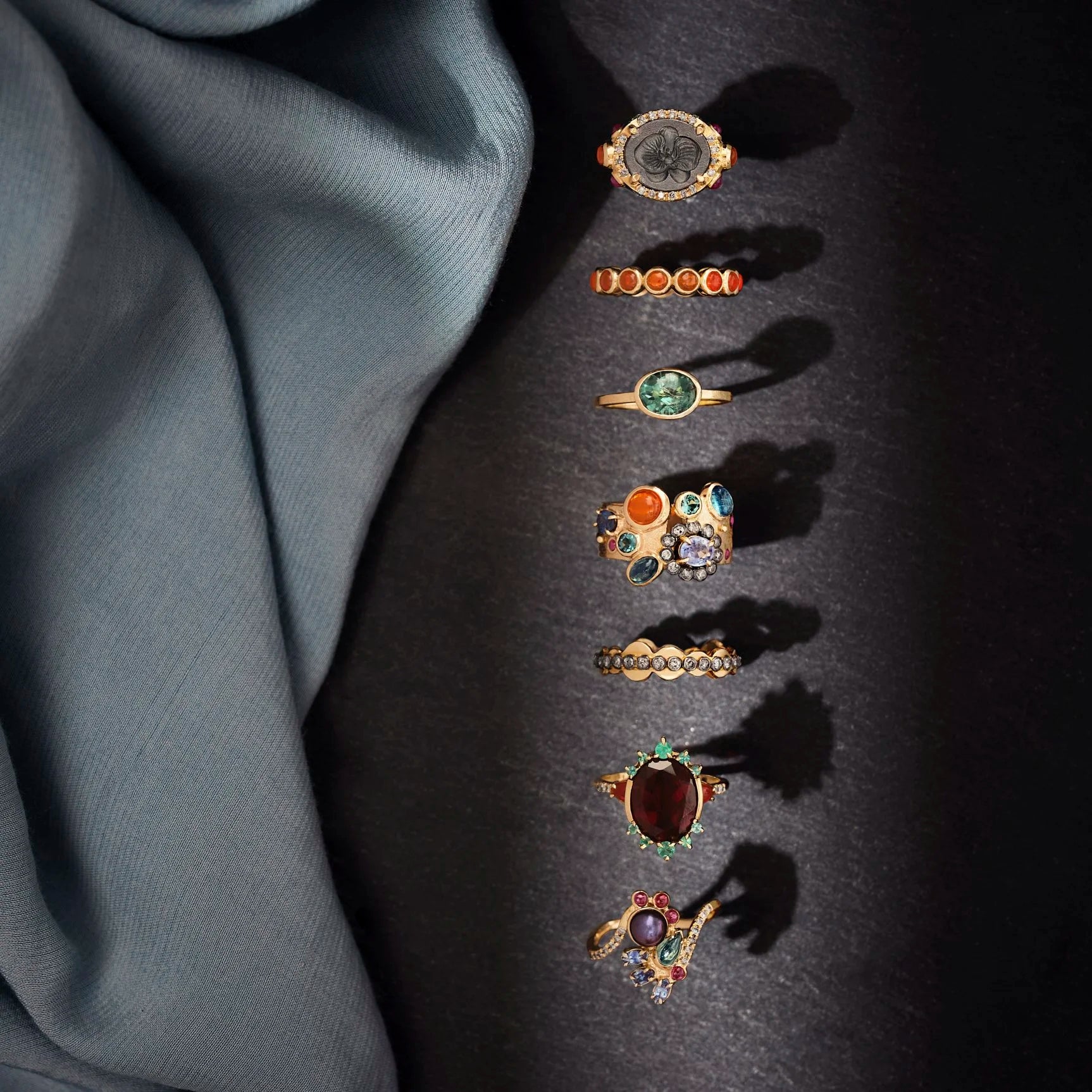 Set of gold rings with various gemstones on a dark surface with gray fabric.