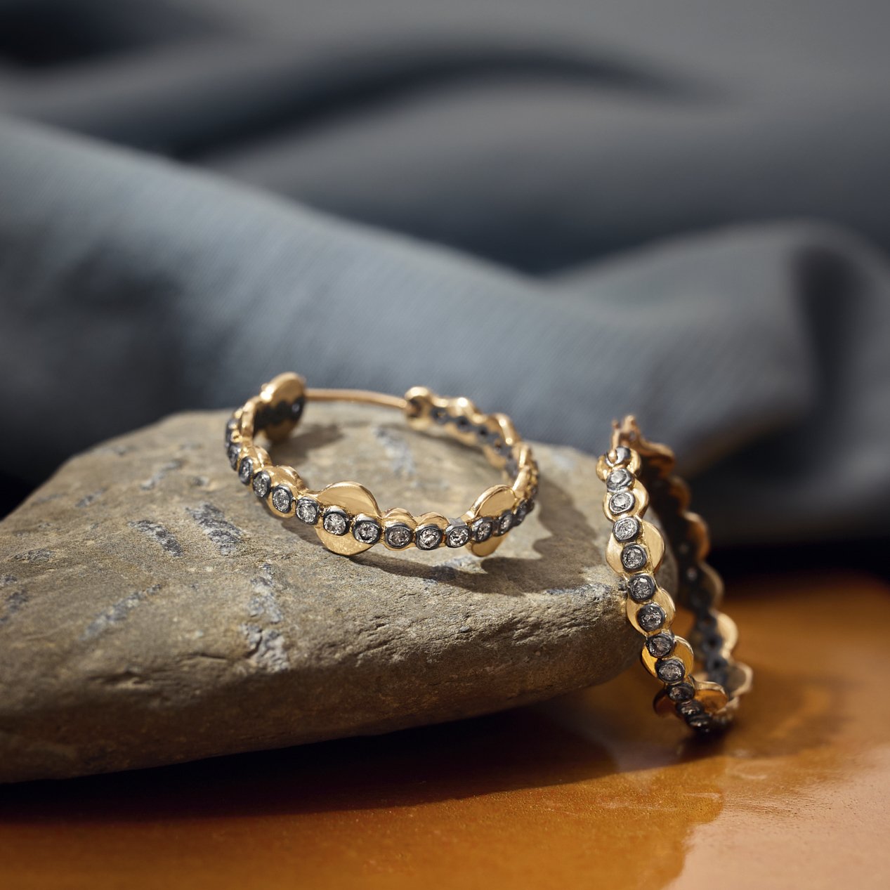 Gold hoop earrings with embedded stones on a stone surface with a gray fabric background