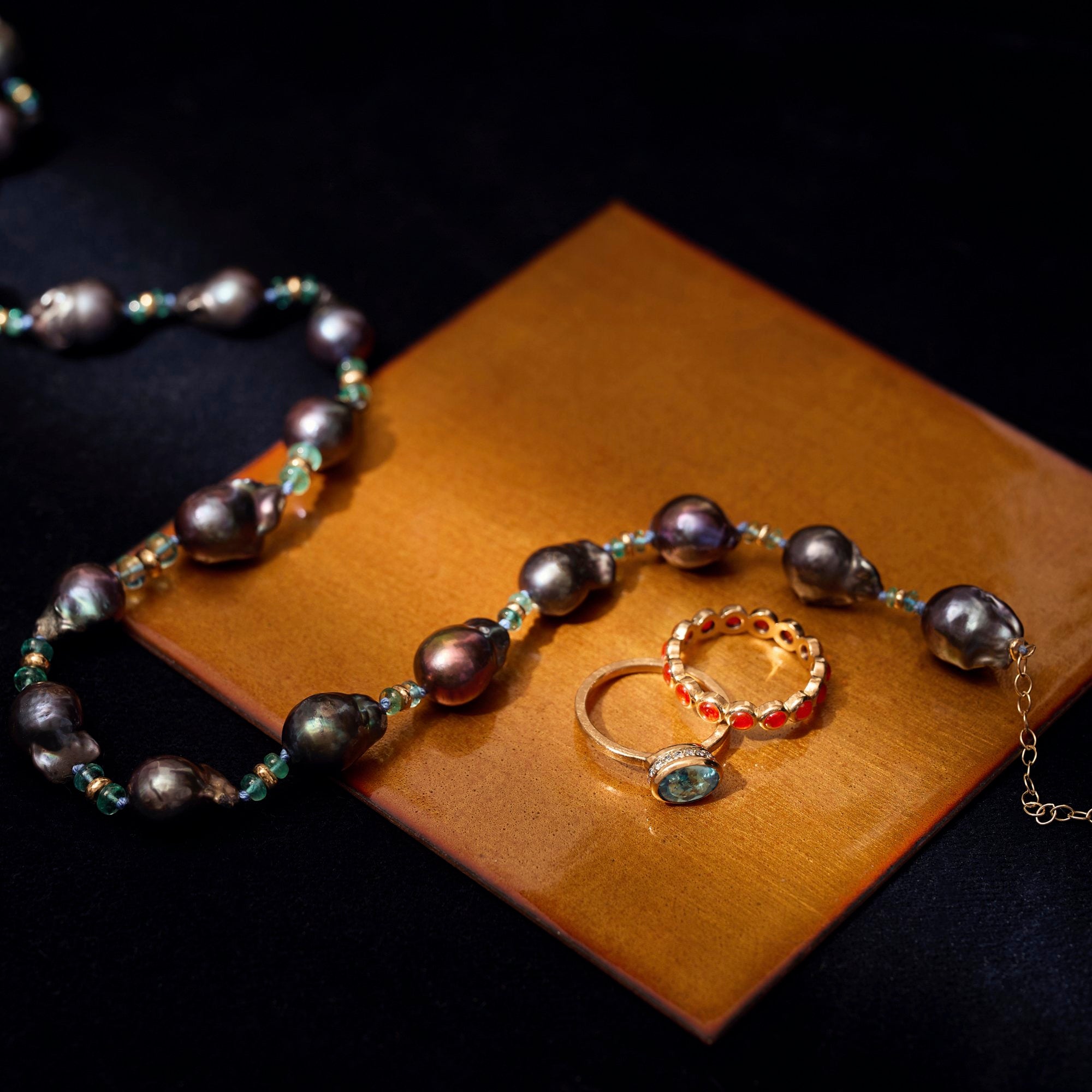 Pearl necklace and two rings on a glass surface with a dark background