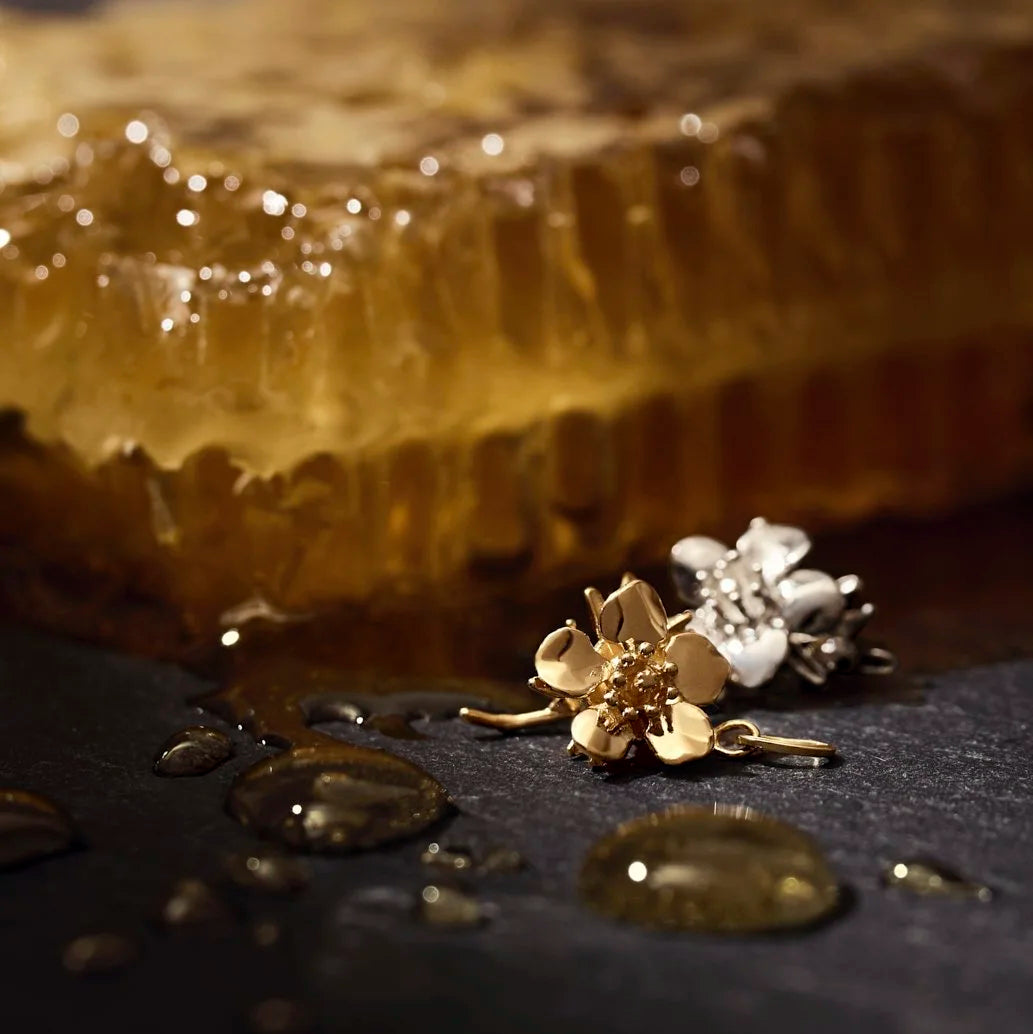 Gold floral earrings on a dark surface with honeycomb in the background