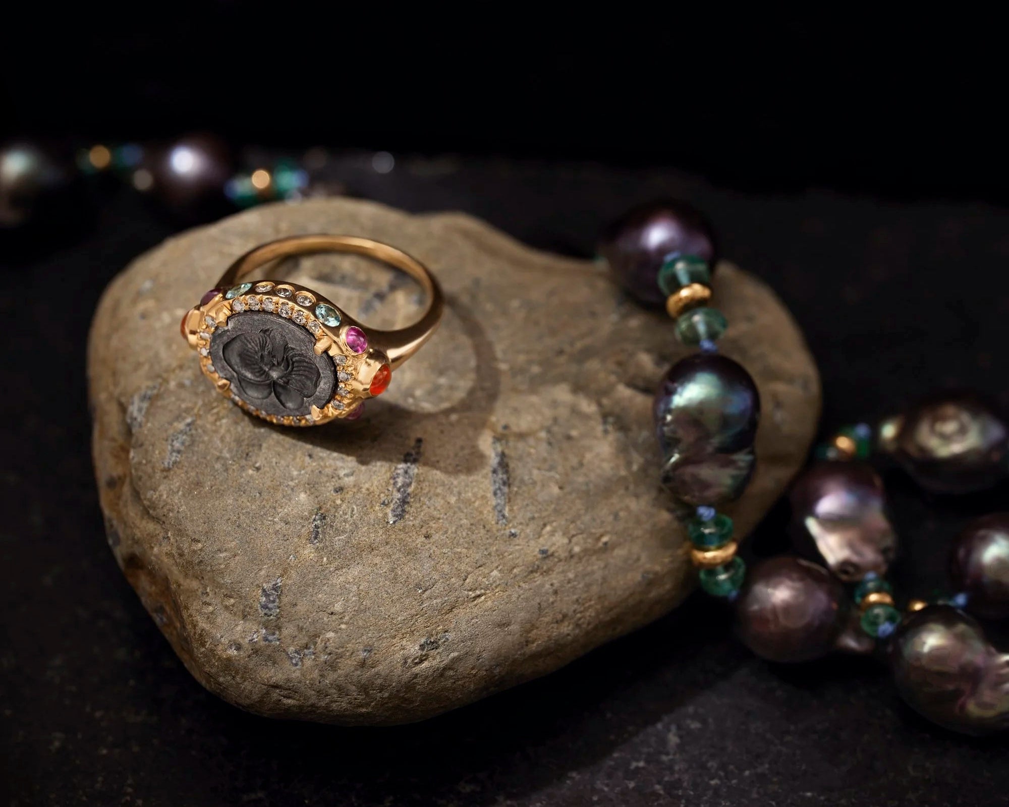 Gold ring with gemstones on a stone with a necklace and pearls in the background