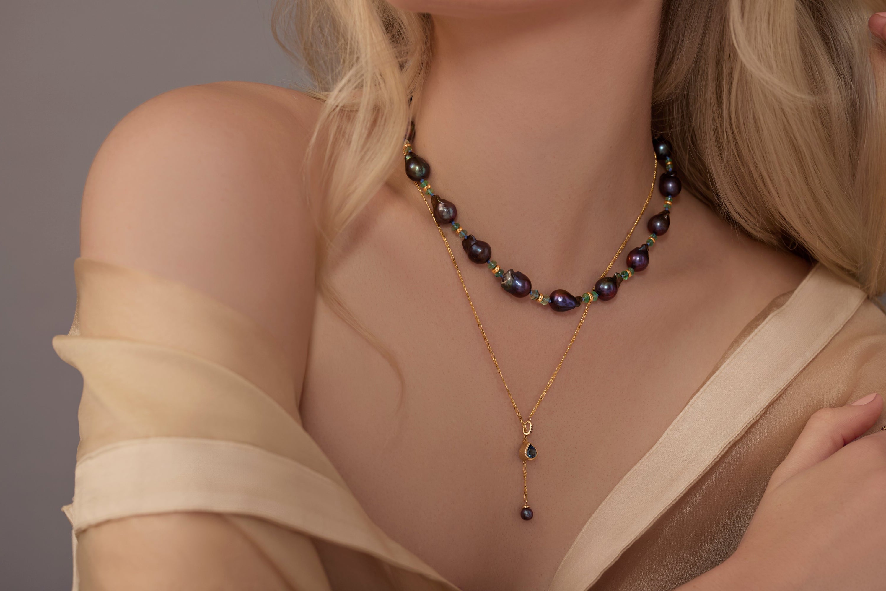 Close-up of a woman wearing a gold pendant necklace with a black pearl strand against a neutral background