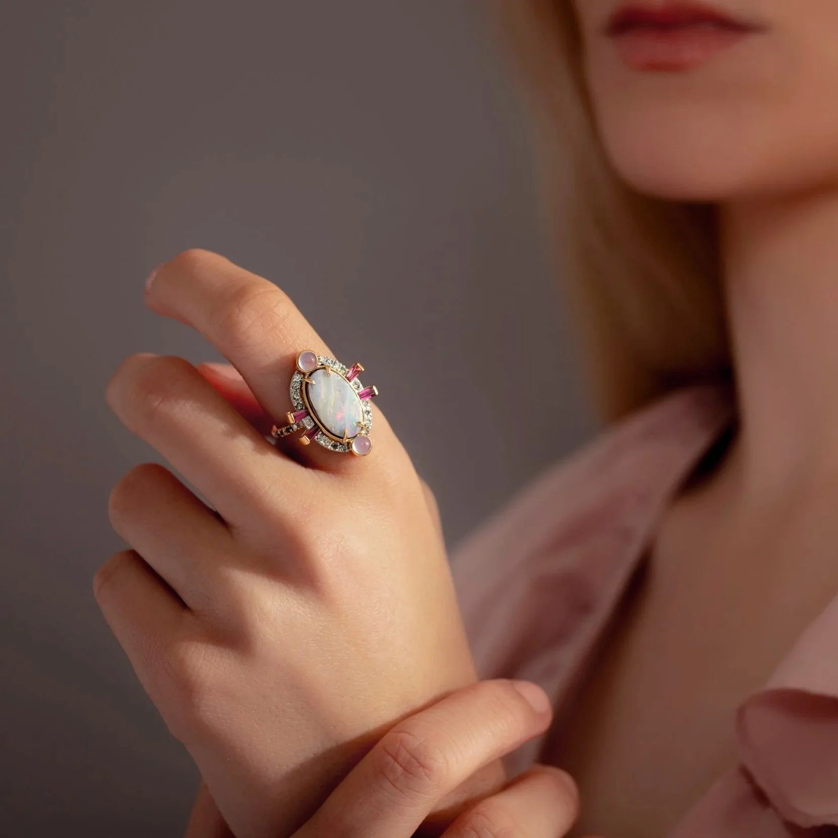 Close-up of a hand wearing an ornate ring with a pink gemstone against a neutral background