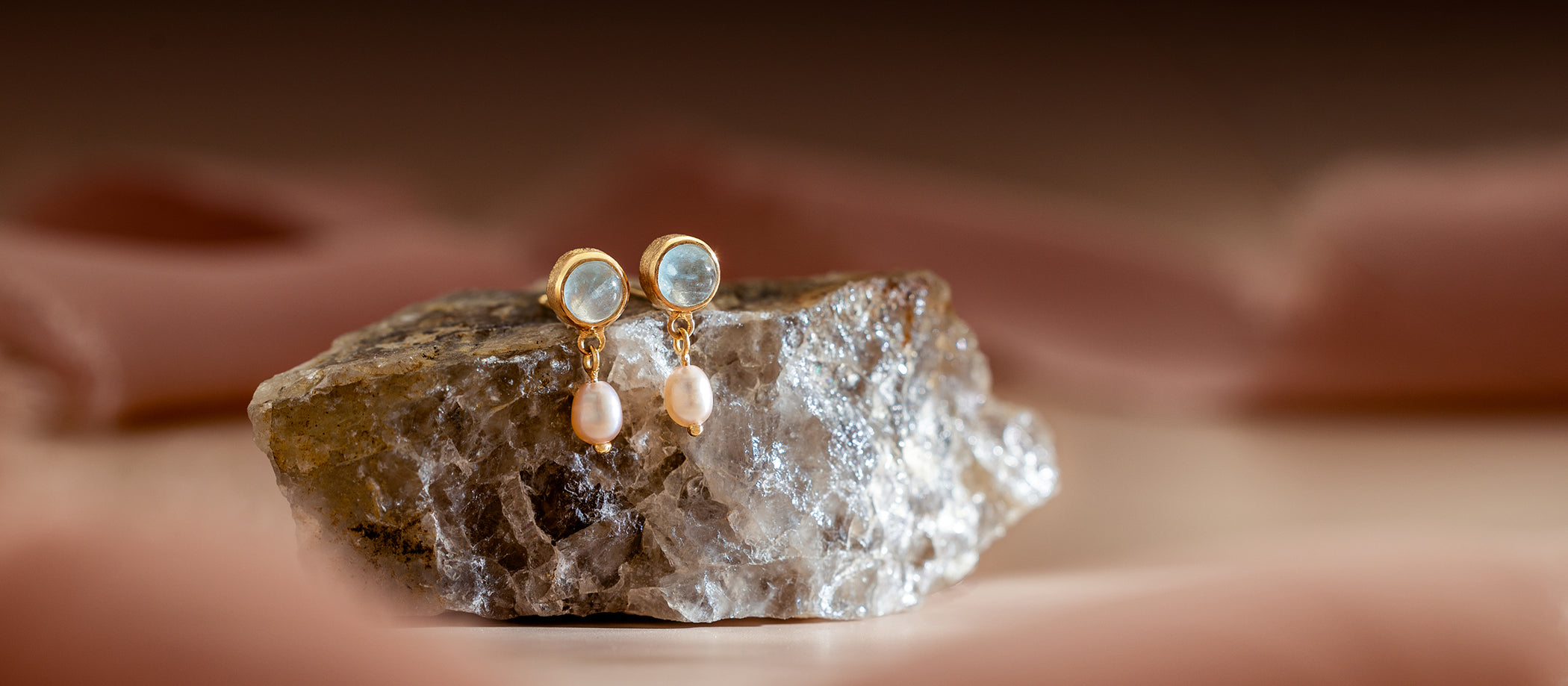 Gold earrings with pearl drops on a rock against a blurred background