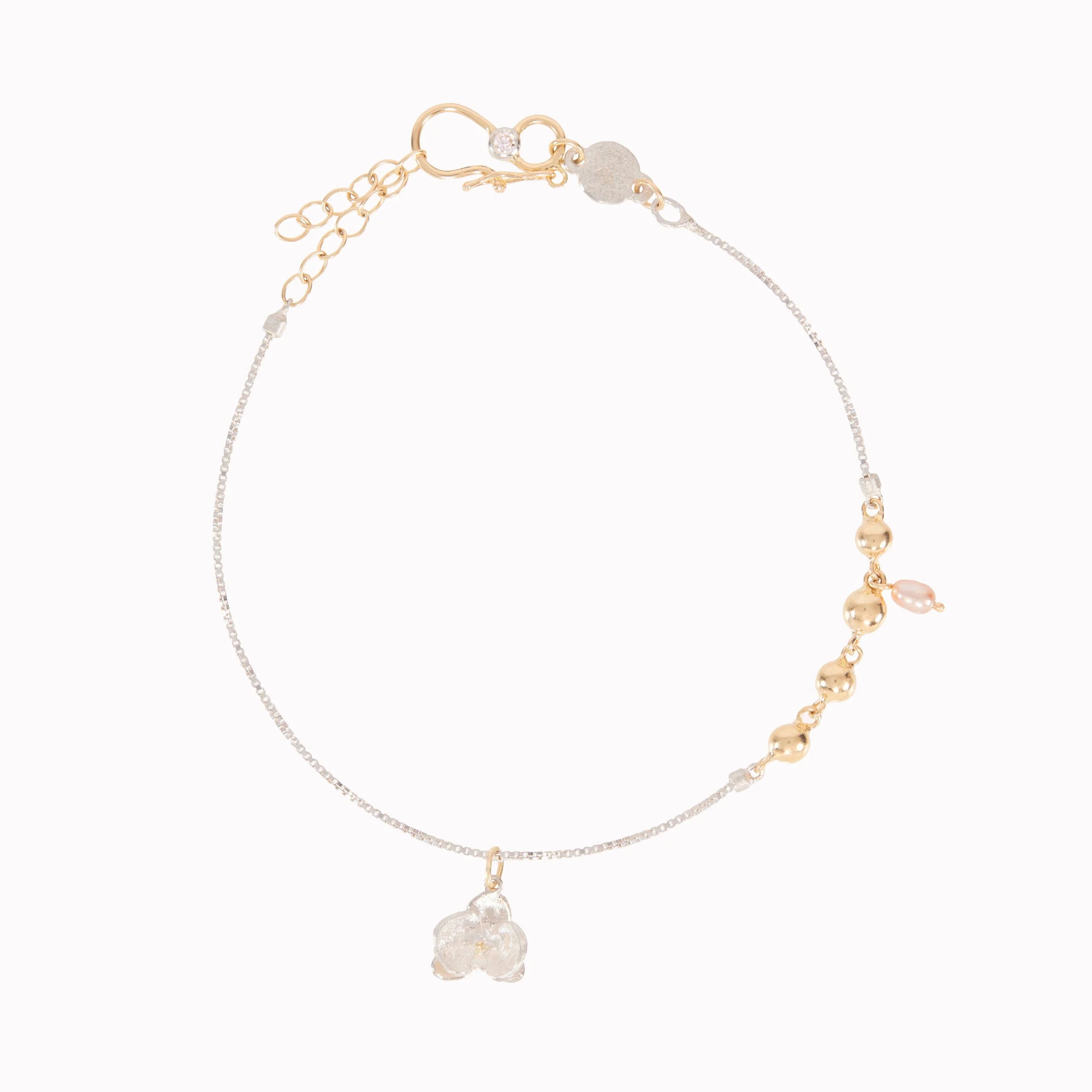 Gold bracelet with small gold beads and a floral charm on a white background
