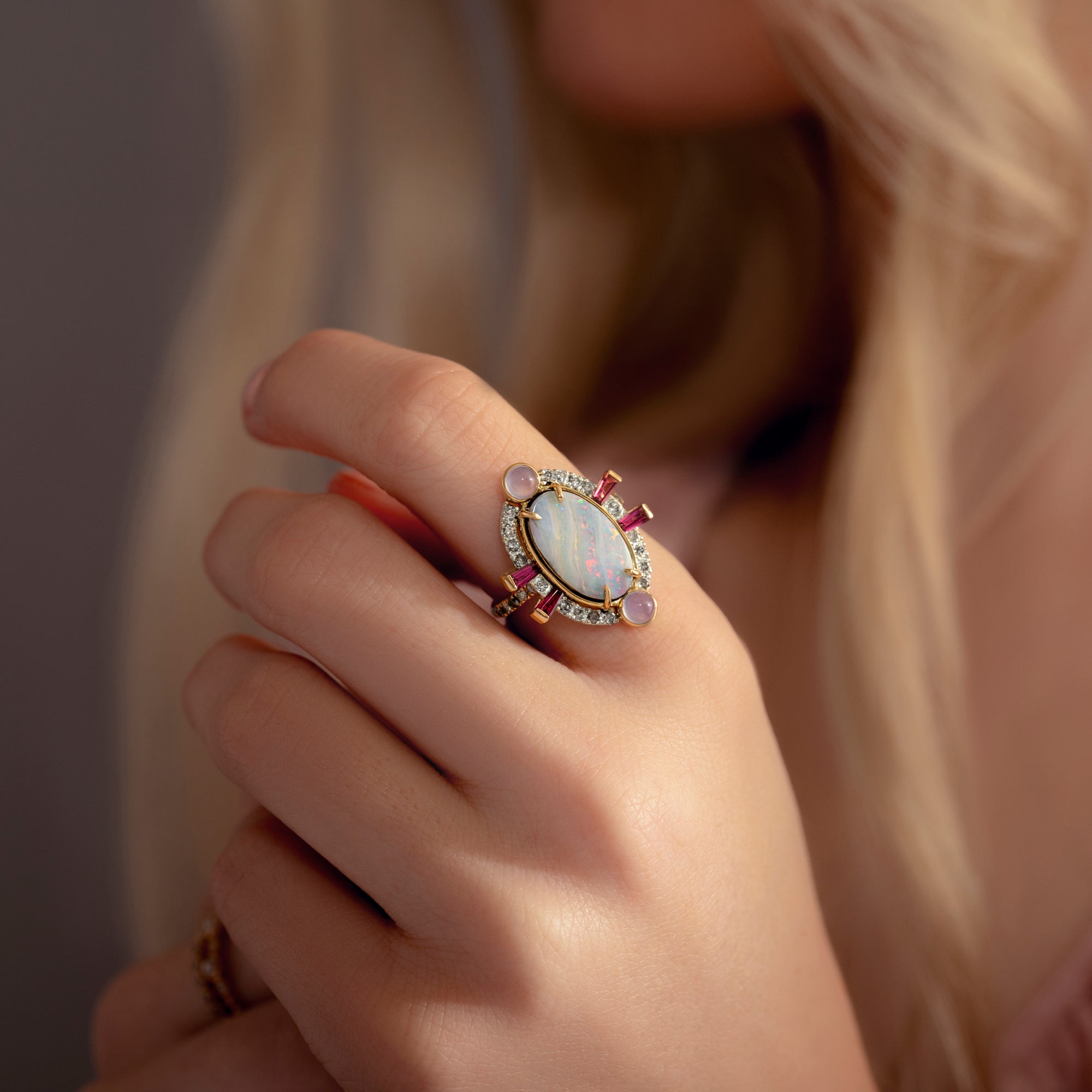 Close-up of a hand wearing an ornate ring with a pink gemstone against a neutral background