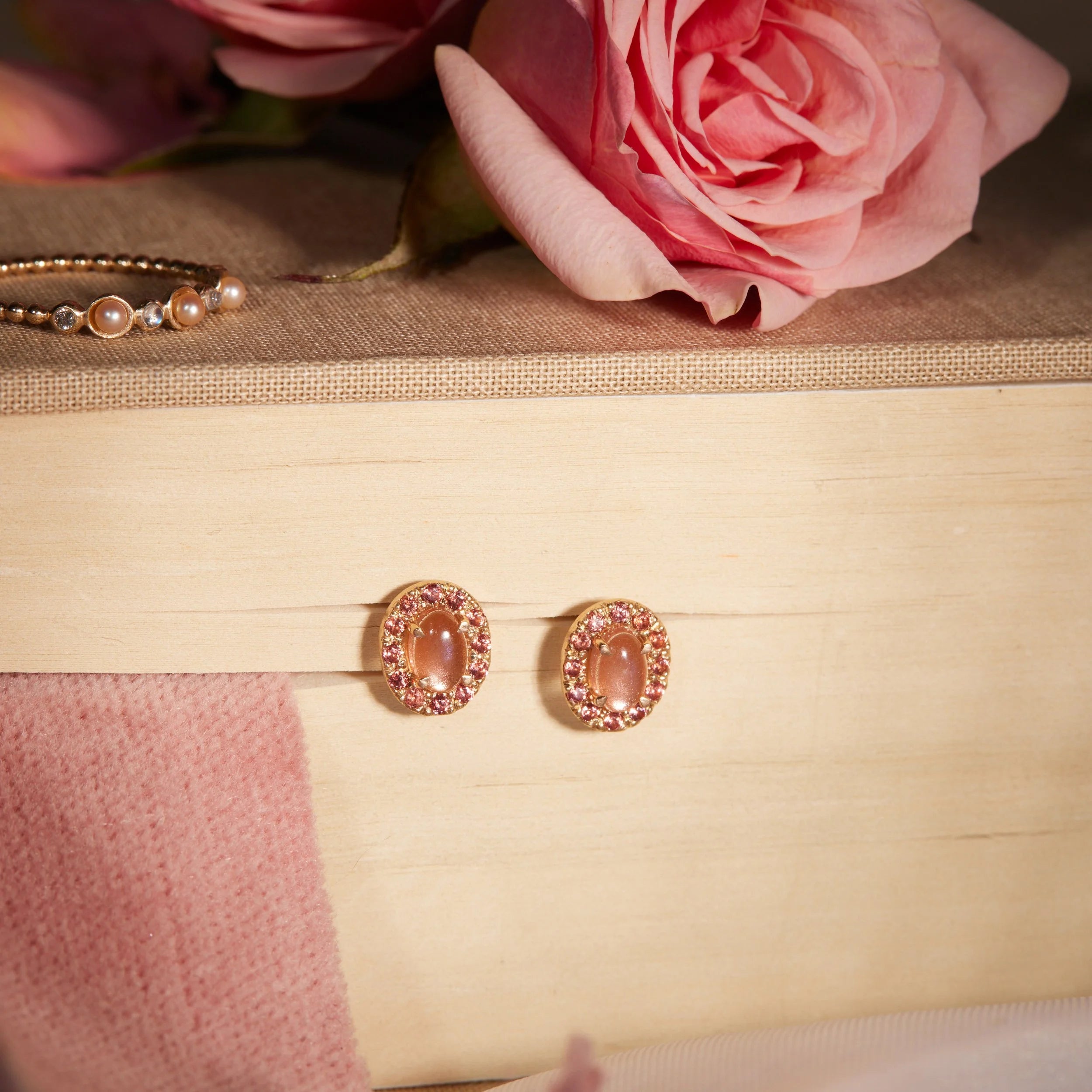 Pair of pink gemstone earrings hanging between book pages with pink flowers in the background