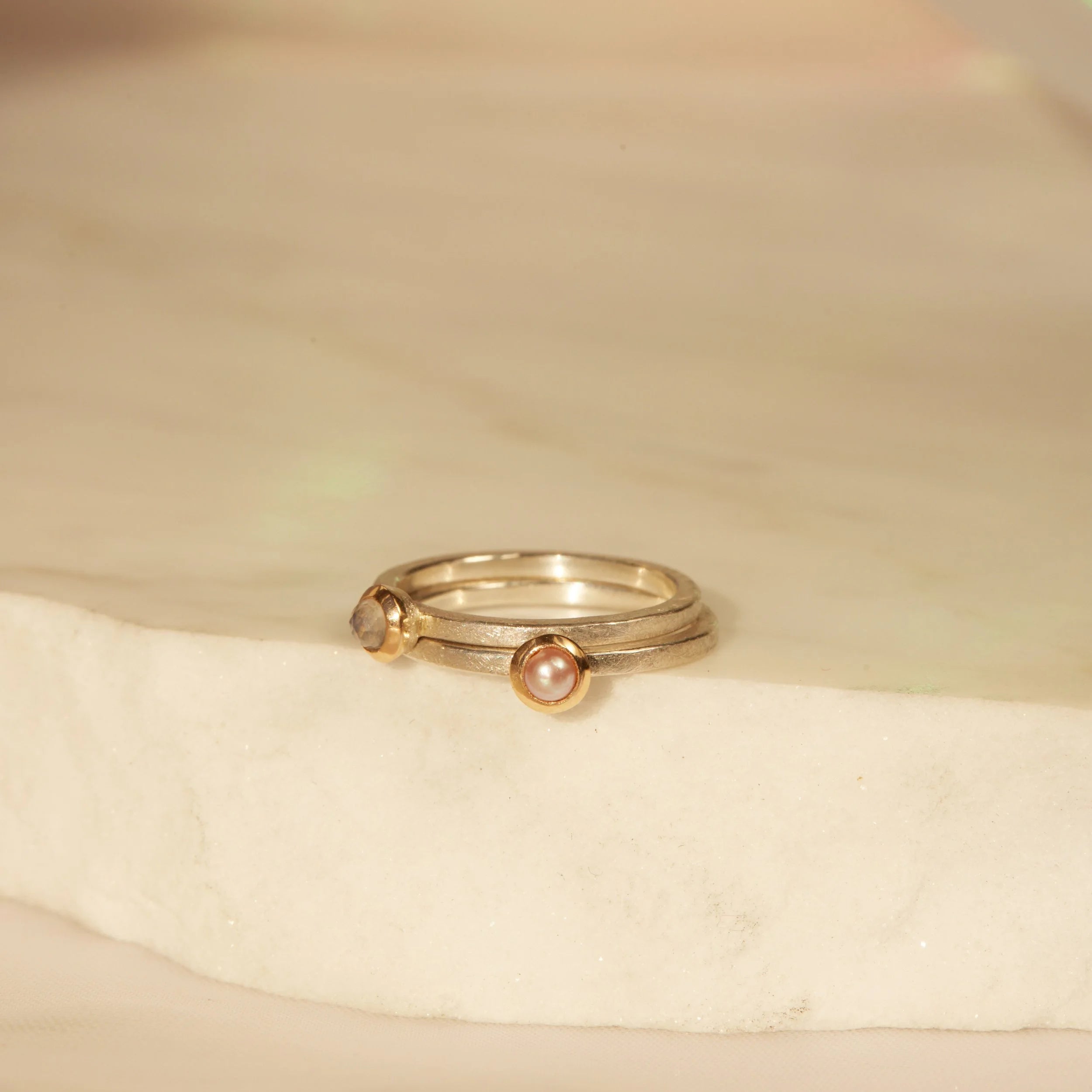 Two silver rings with gemstones on a beige fabric background
