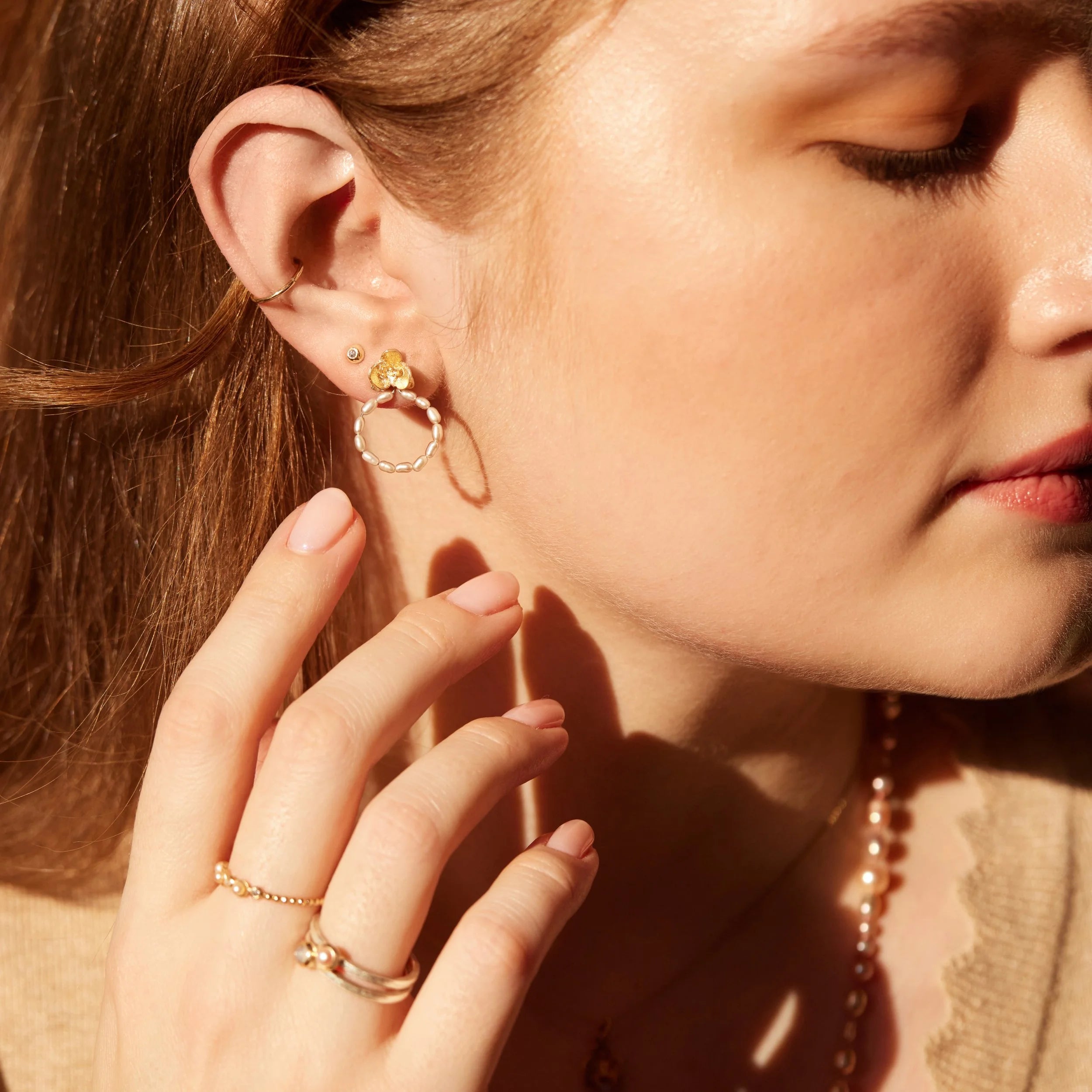 Close-up of a woman wearing gold hoop earrings and rings, with a warm, soft focus.