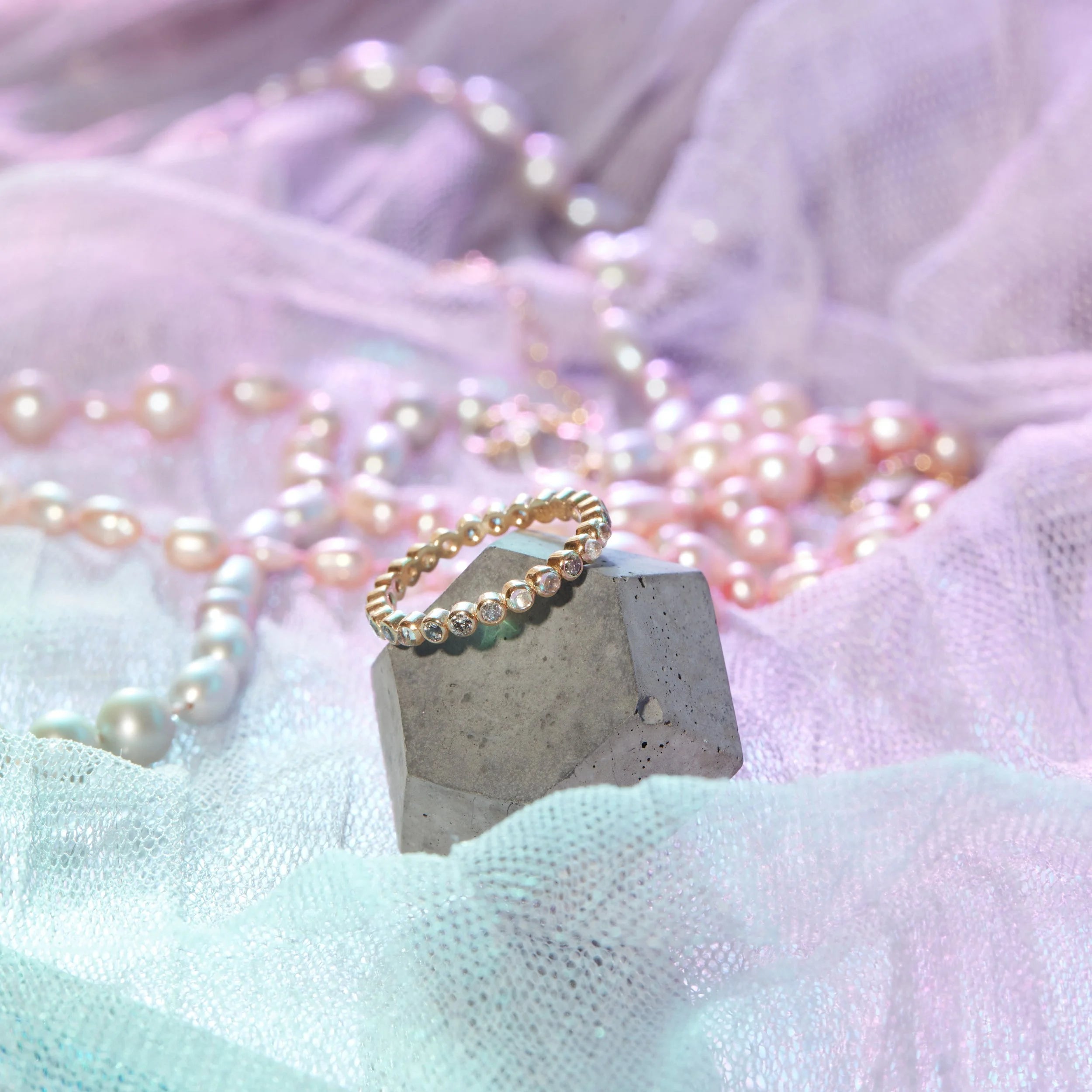 Gold ring on a concrete block with pink pearls in the background