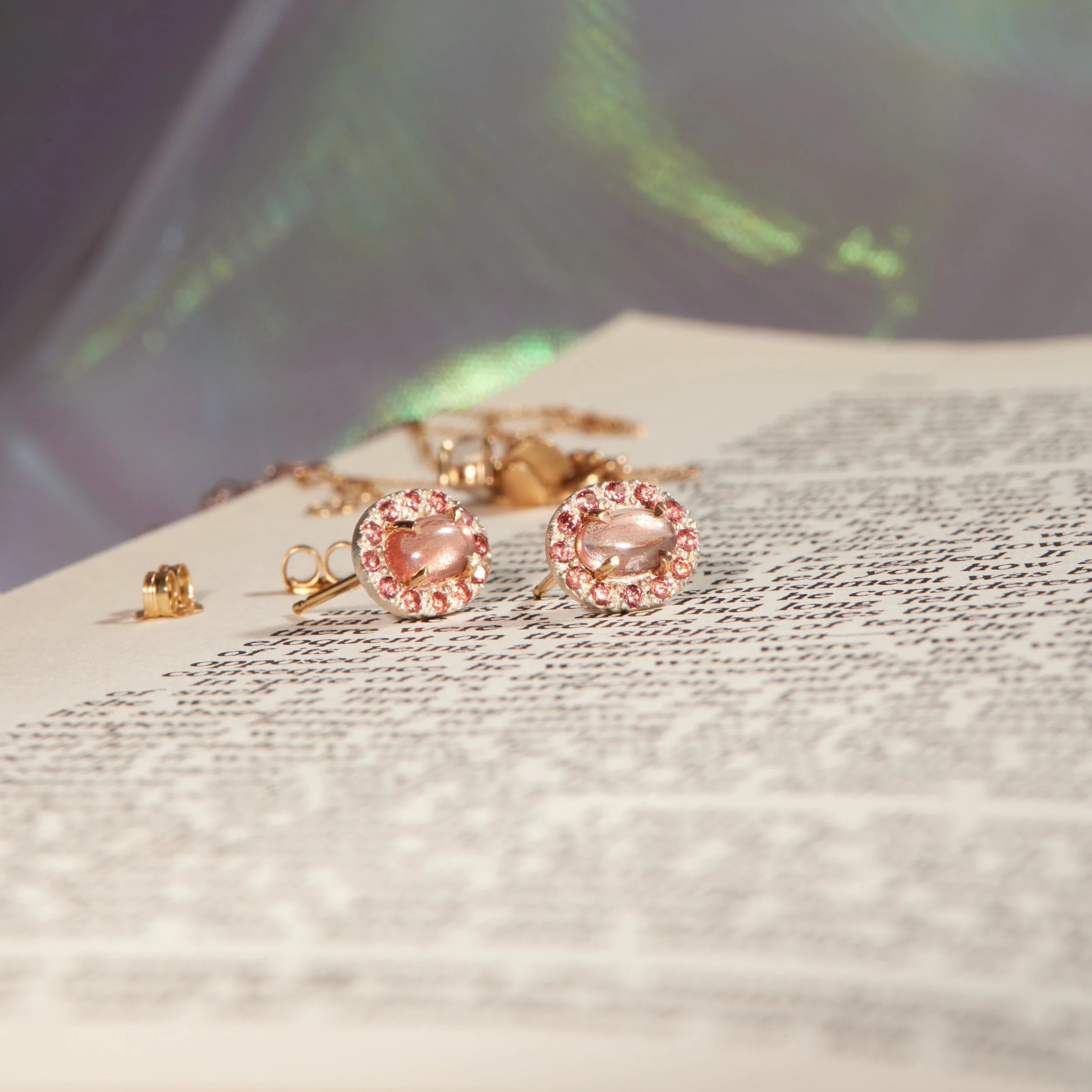 Pair of gold earrings with pink gemstones on a textured surface