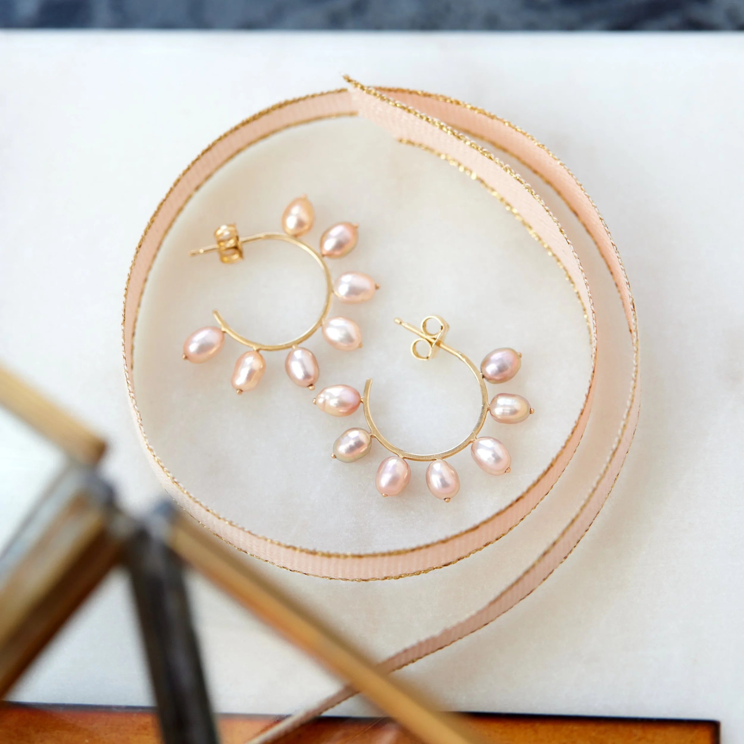 Pair of pearl hoop earrings on a round beige mat with a blurred background
