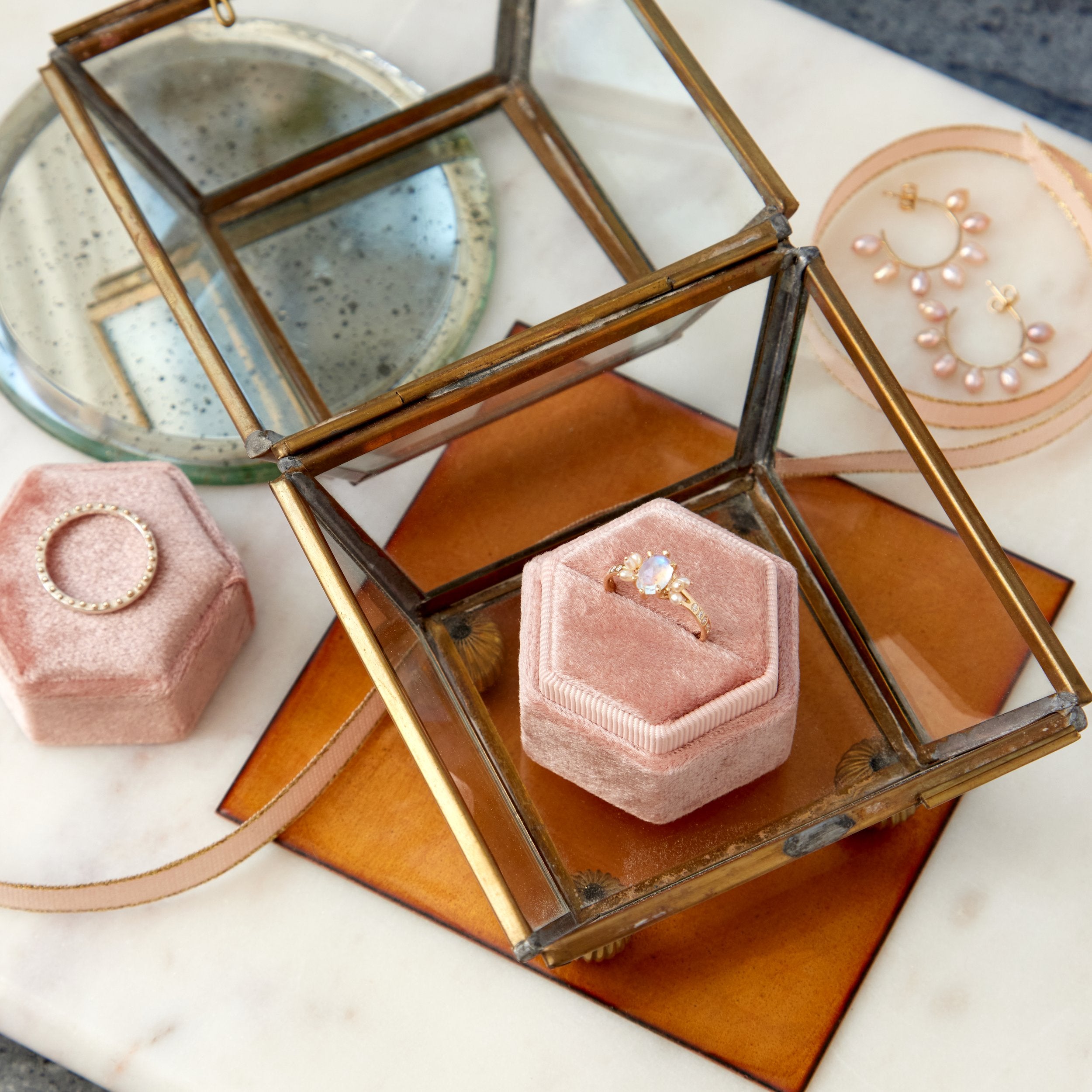 Gold ring on a pink velvet ring box inside a glass jewelry box with a marble surface.