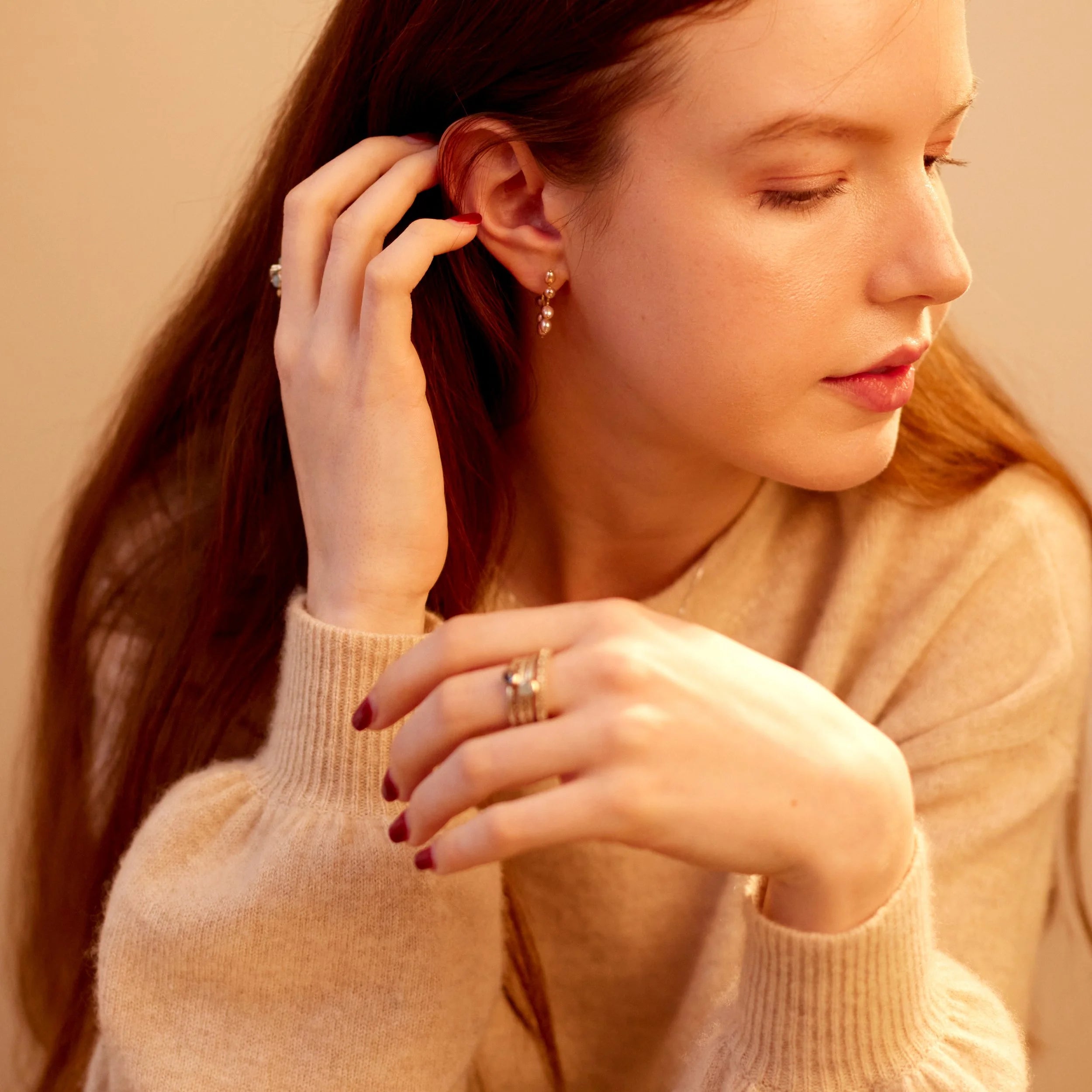 Woman adjusting an earring against a beige background