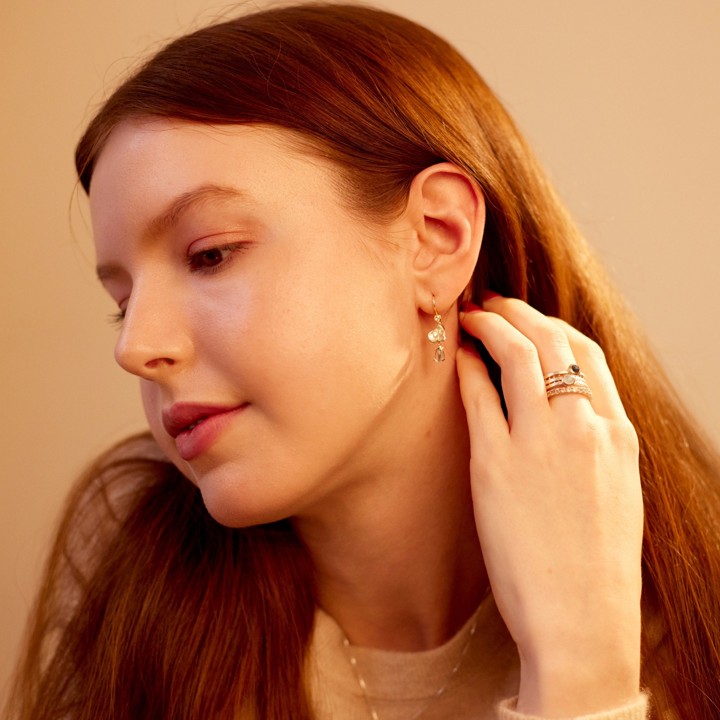 Woman adjusting an earring with a soft beige background