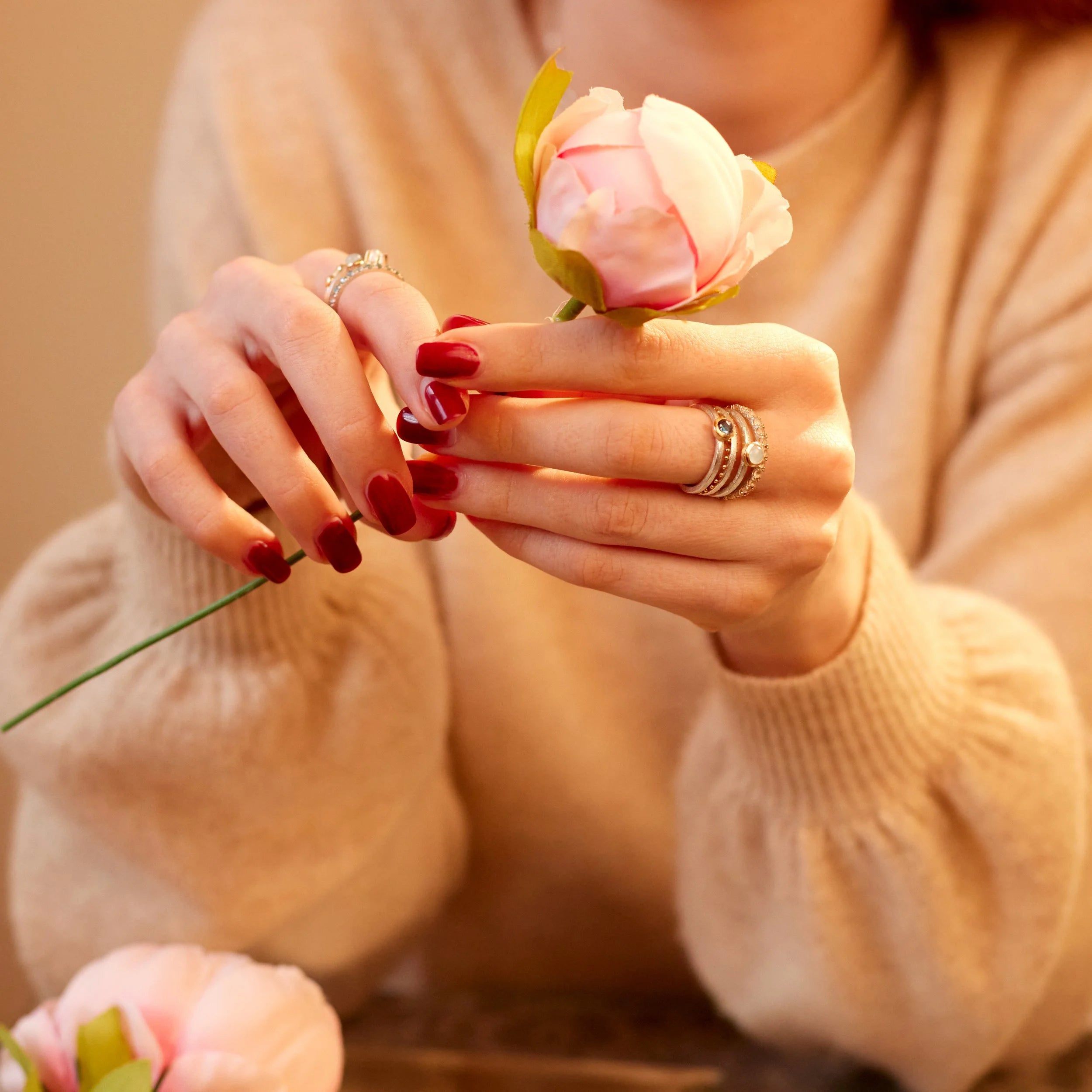 Close-up of hands holding a small pink flower with a blurred background