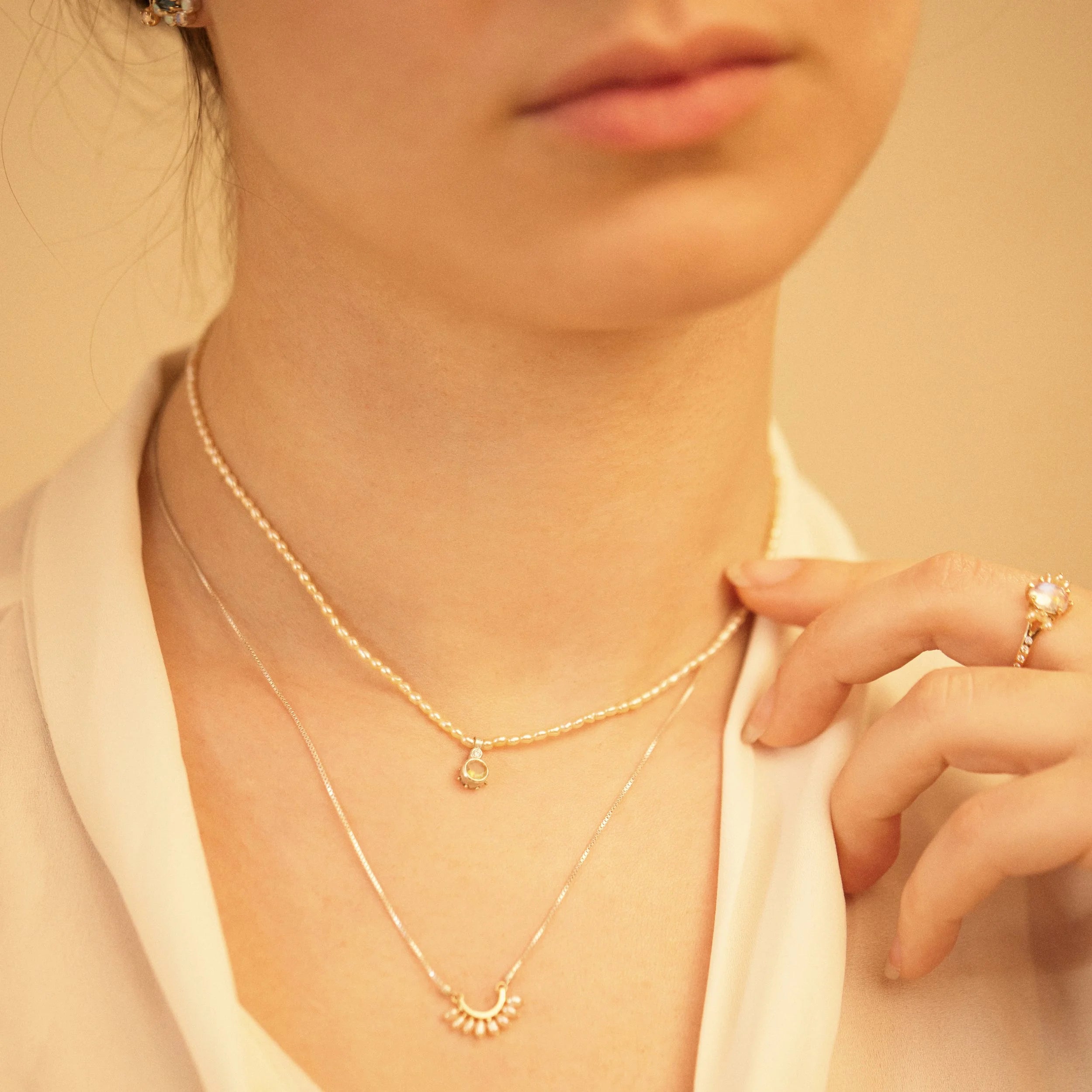 Close-up of a person wearing a delicate gold necklace and ring on a soft beige background