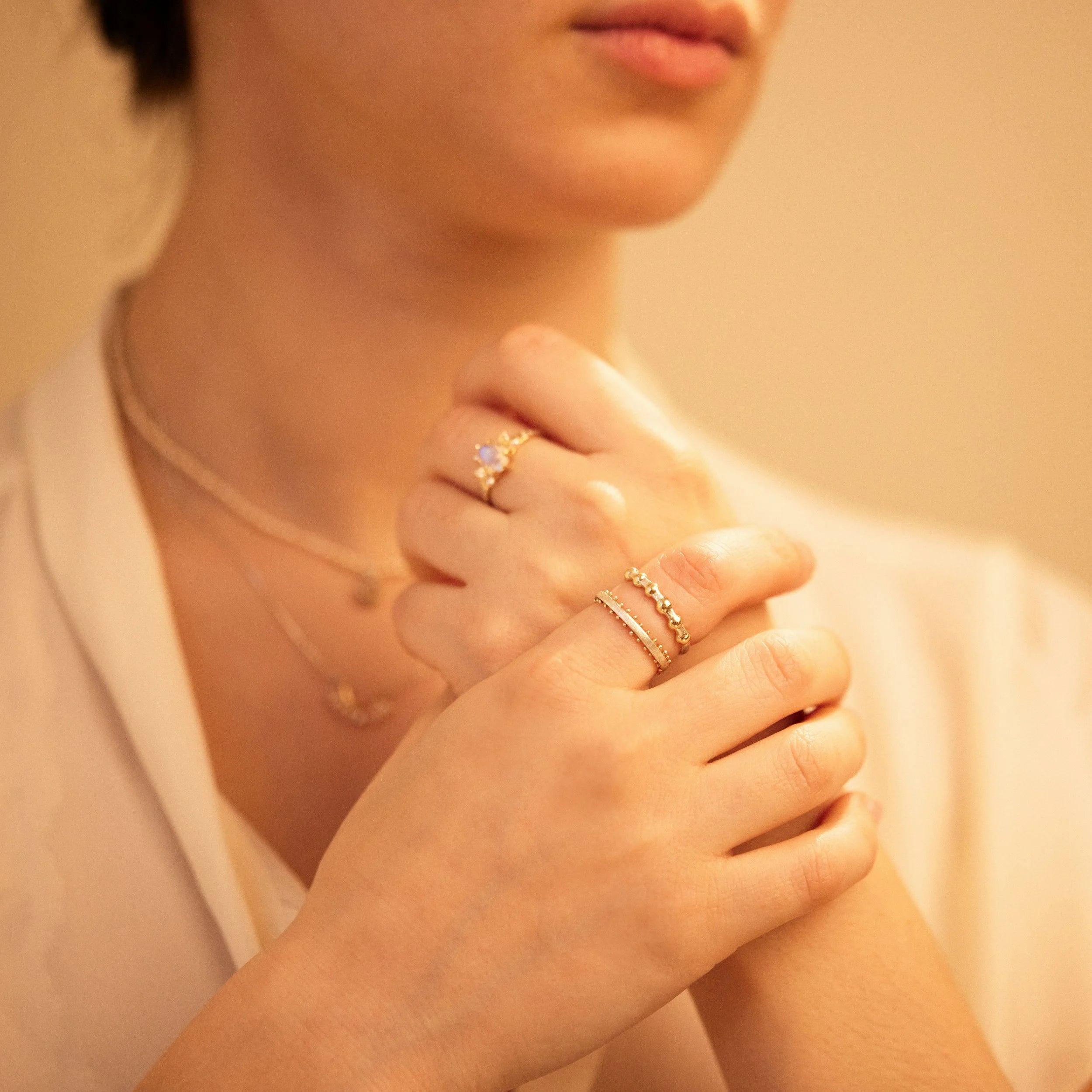 Close-up of a person's hands with rings, wearing a white blouse.