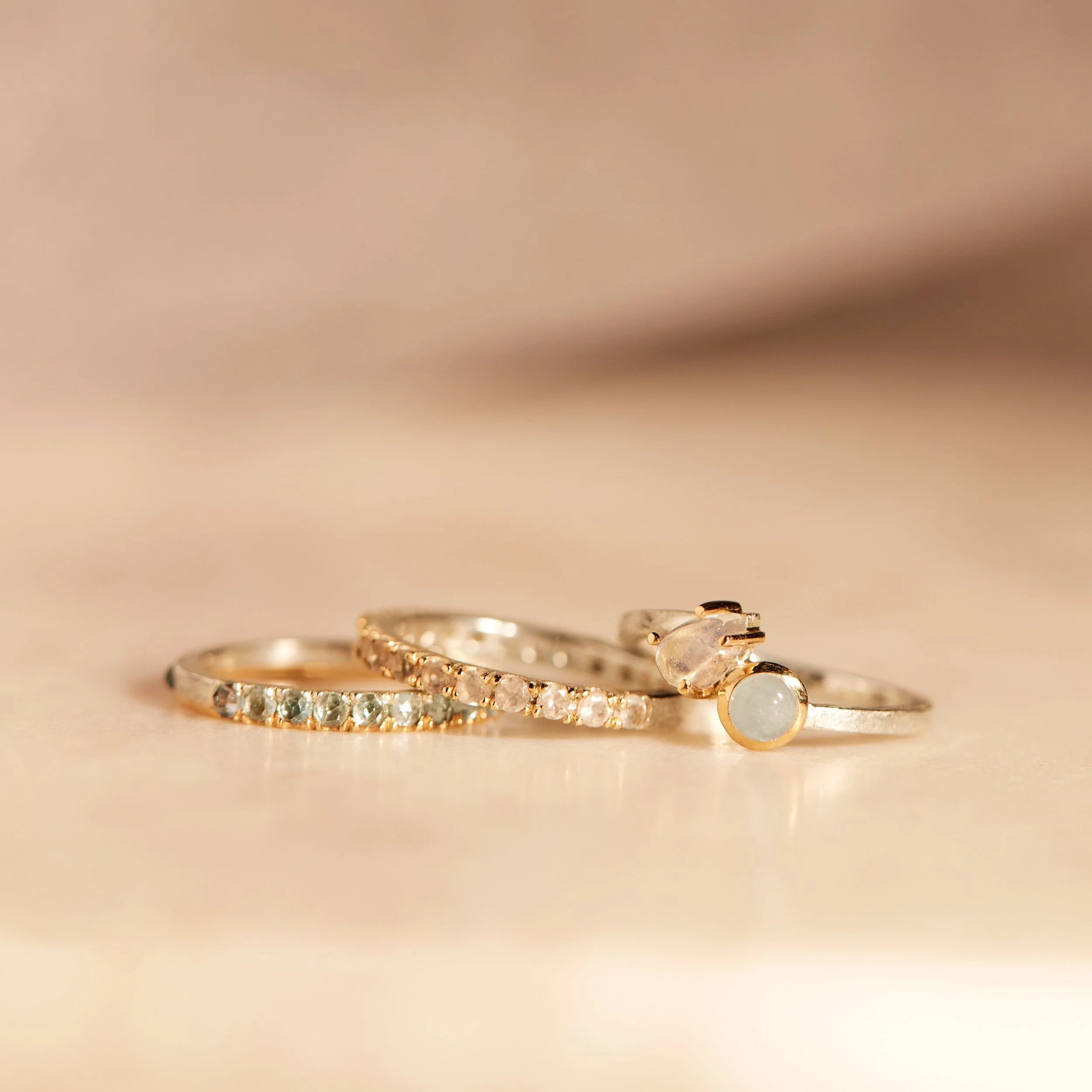 Three gold rings with gemstones on a beige background
