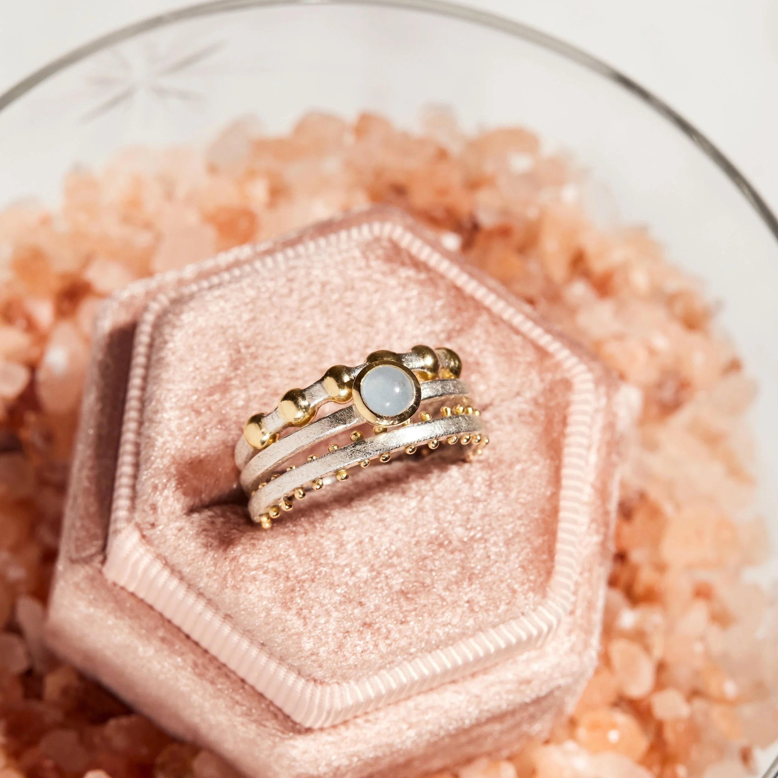 Gold ring with a central gemstone on a pink velvet stand with pink salt crystals.