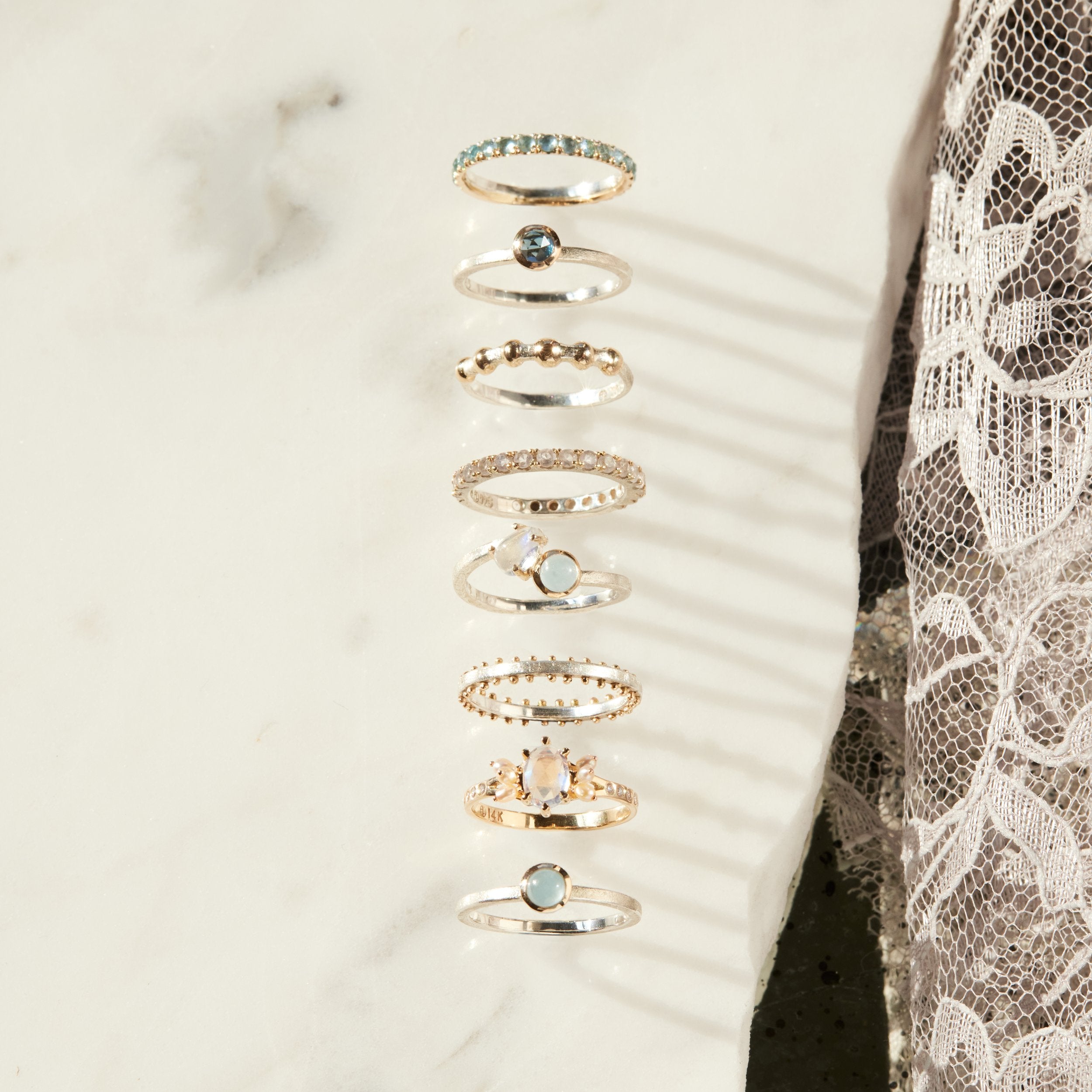 Set of gold rings with gemstones on a white slab and lace background