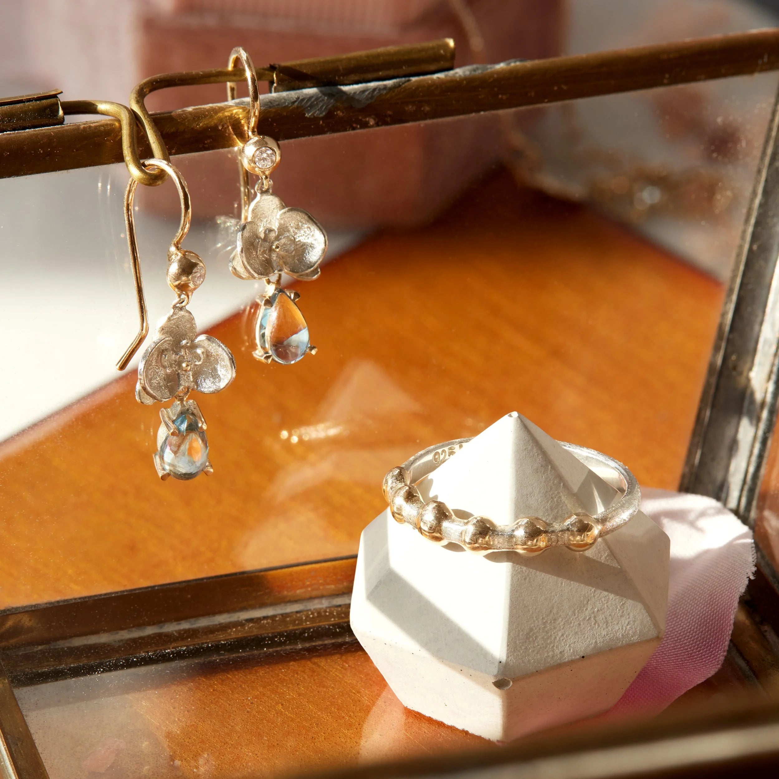 Gold earrings and ring on a glass surface with a blurred background