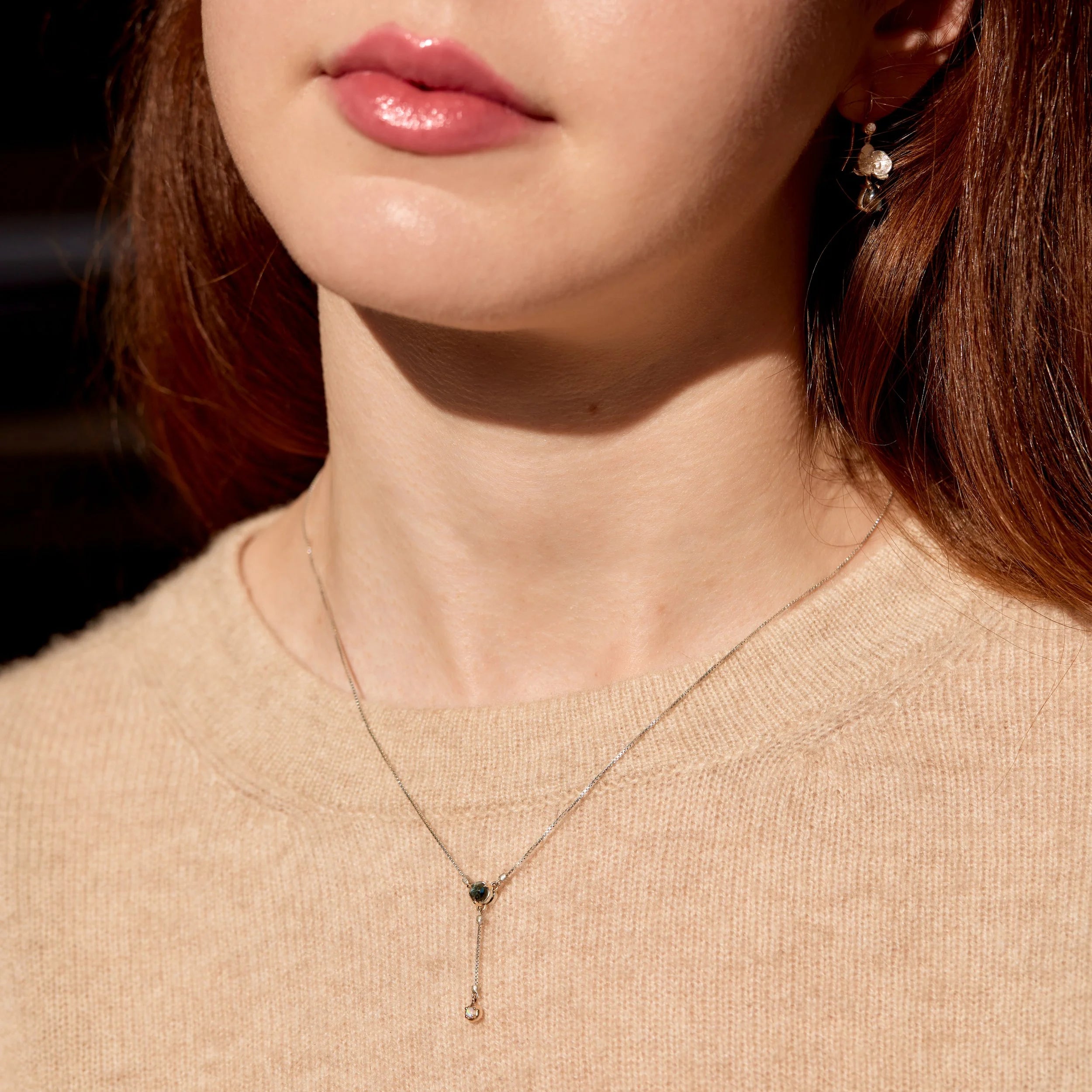 Close-up of a woman wearing a delicate necklace with a dark stone.