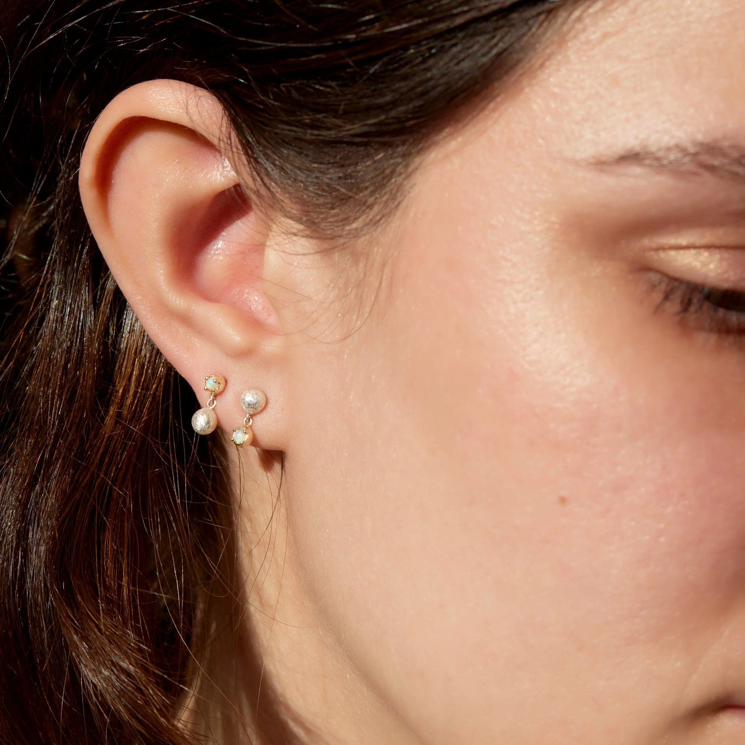 Close-up of a person wearing opal earrings with a blurred background